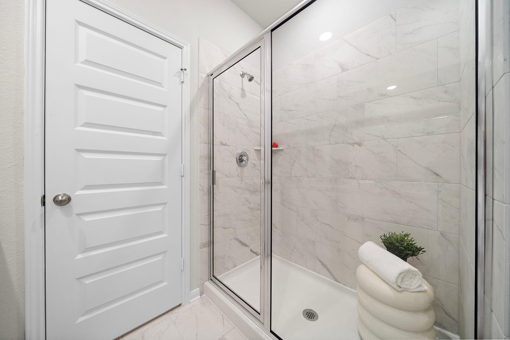 Modern bathroom with glass shower at Liberty Estates in Cleveland Texas featuring white subway tiles potted plant and rolled towels