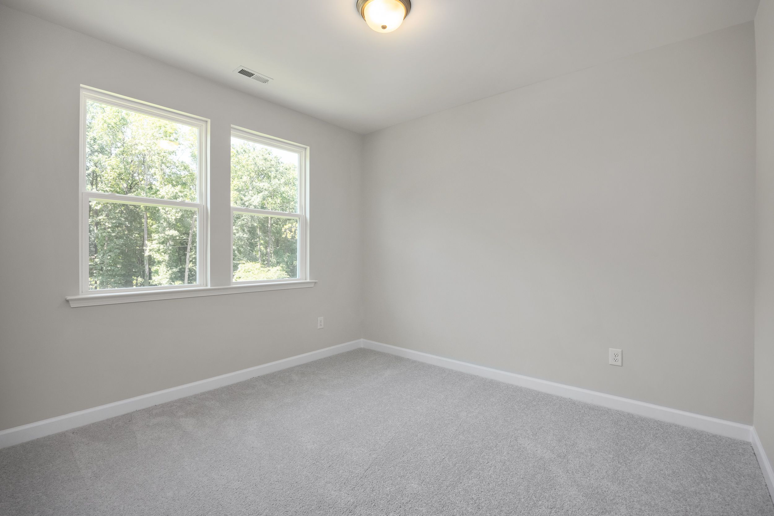 Upper floor bedroom in The Aspen C with light gray walls, double windows overlooking trees, and neutral carpet