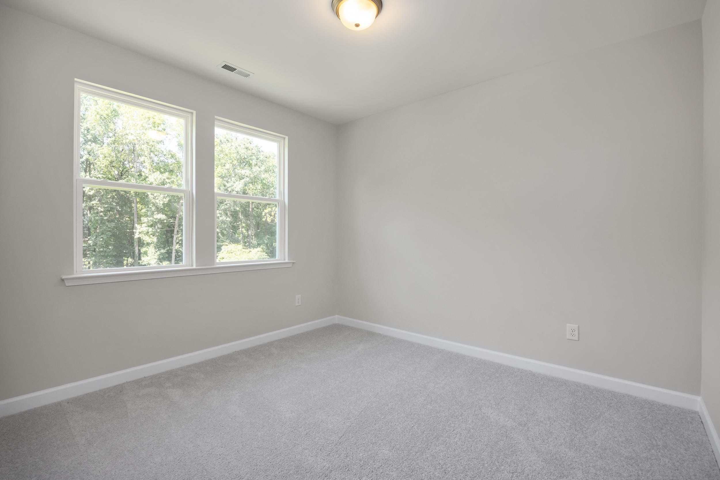 Upper floor bedroom in The Aspen C with light gray walls, double windows overlooking trees, and neutral carpet