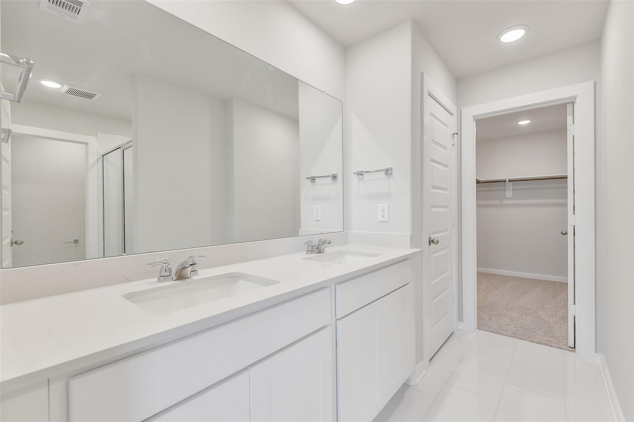 Modern master bathroom featuring double white vanity, large mirror, and open walk-in closet in Davidson Homes The Trinity F, Magnolia, Texas