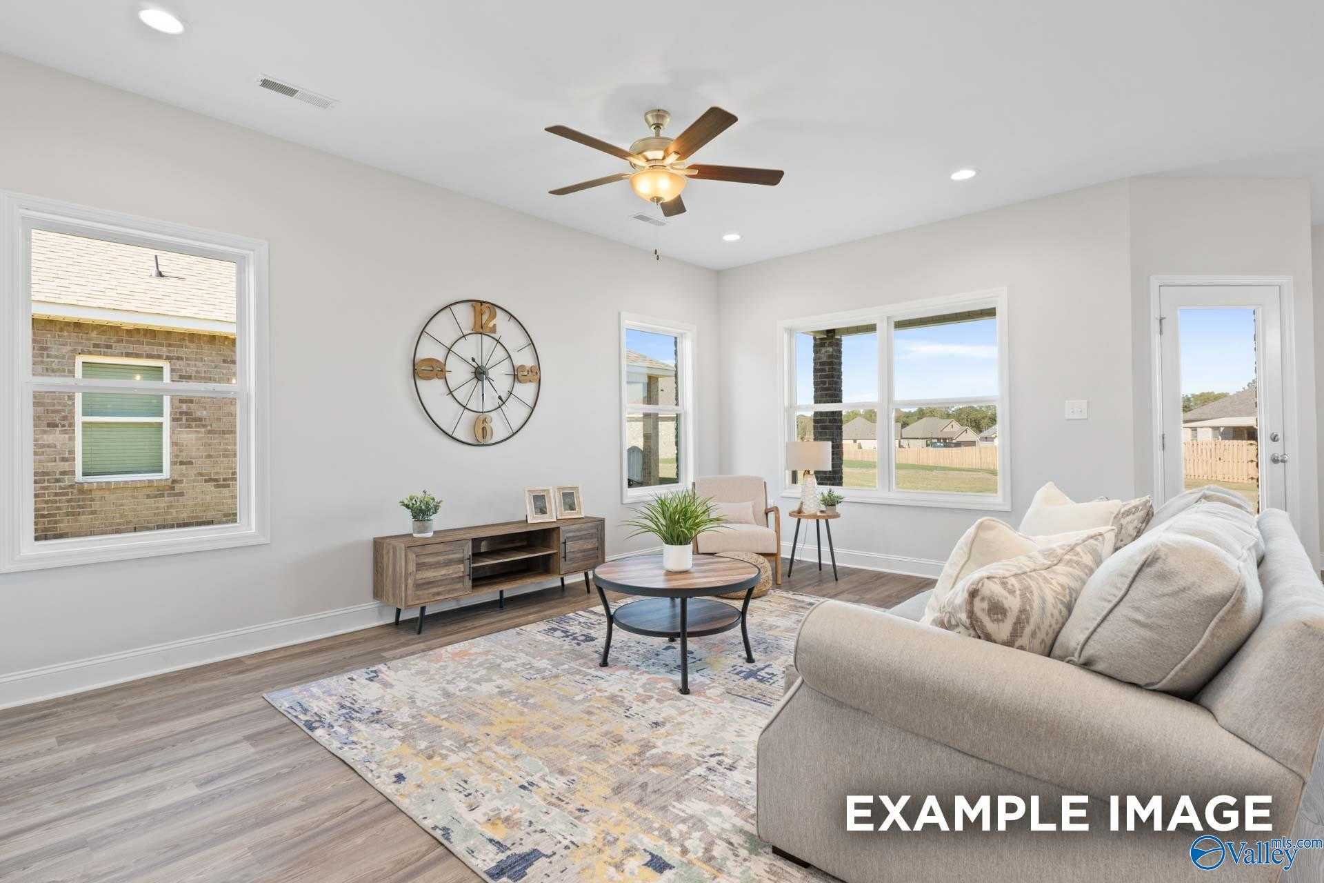 Cozy living room with large windows overlooking yard, beige sofa, ceiling fan, and hardwood floors in Davidson Homes The Franklin C, Meridianville, Alabama