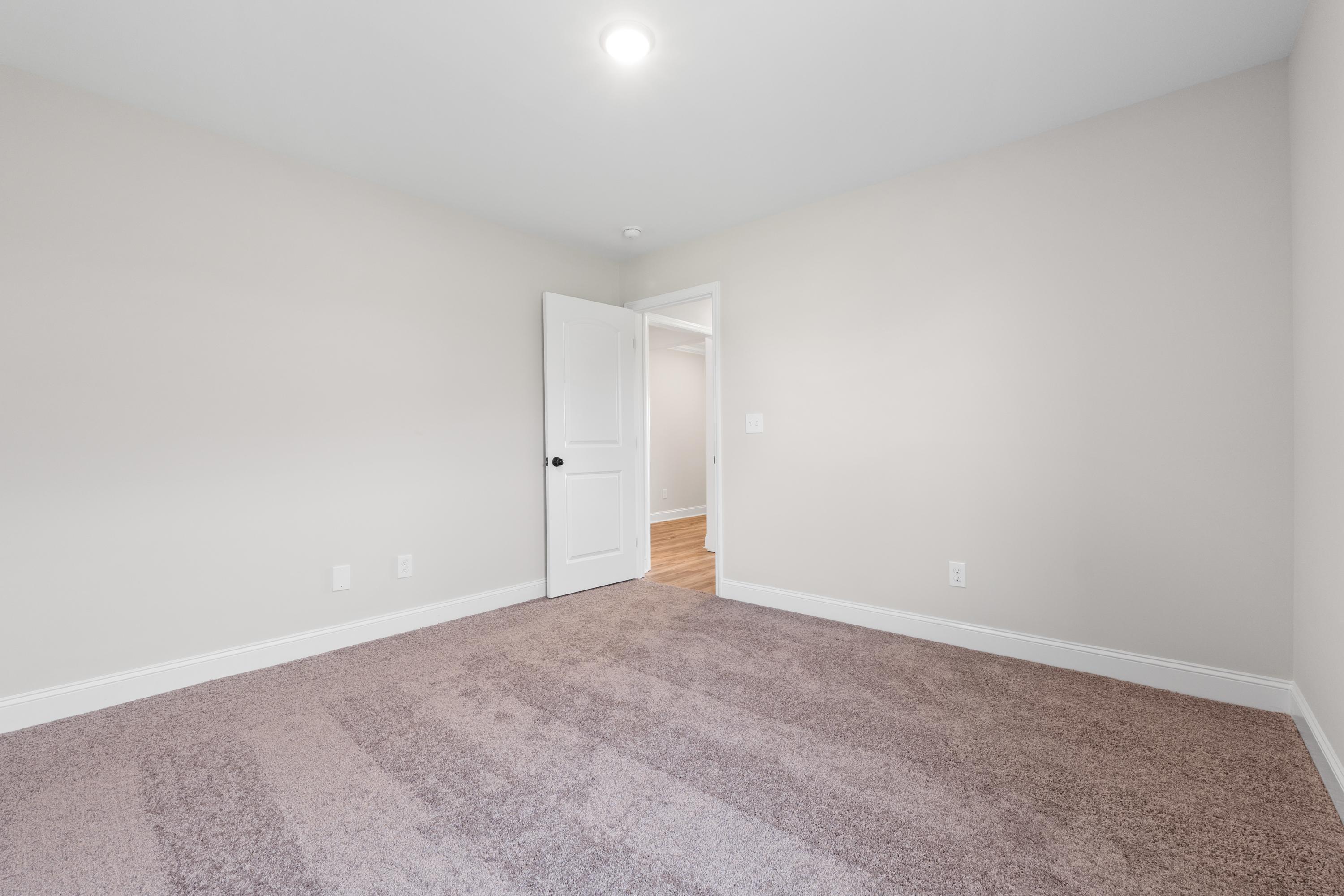 Spacious empty bedroom in The Everett home with beige walls, plush brown carpet, open white door, and recessed ceiling light