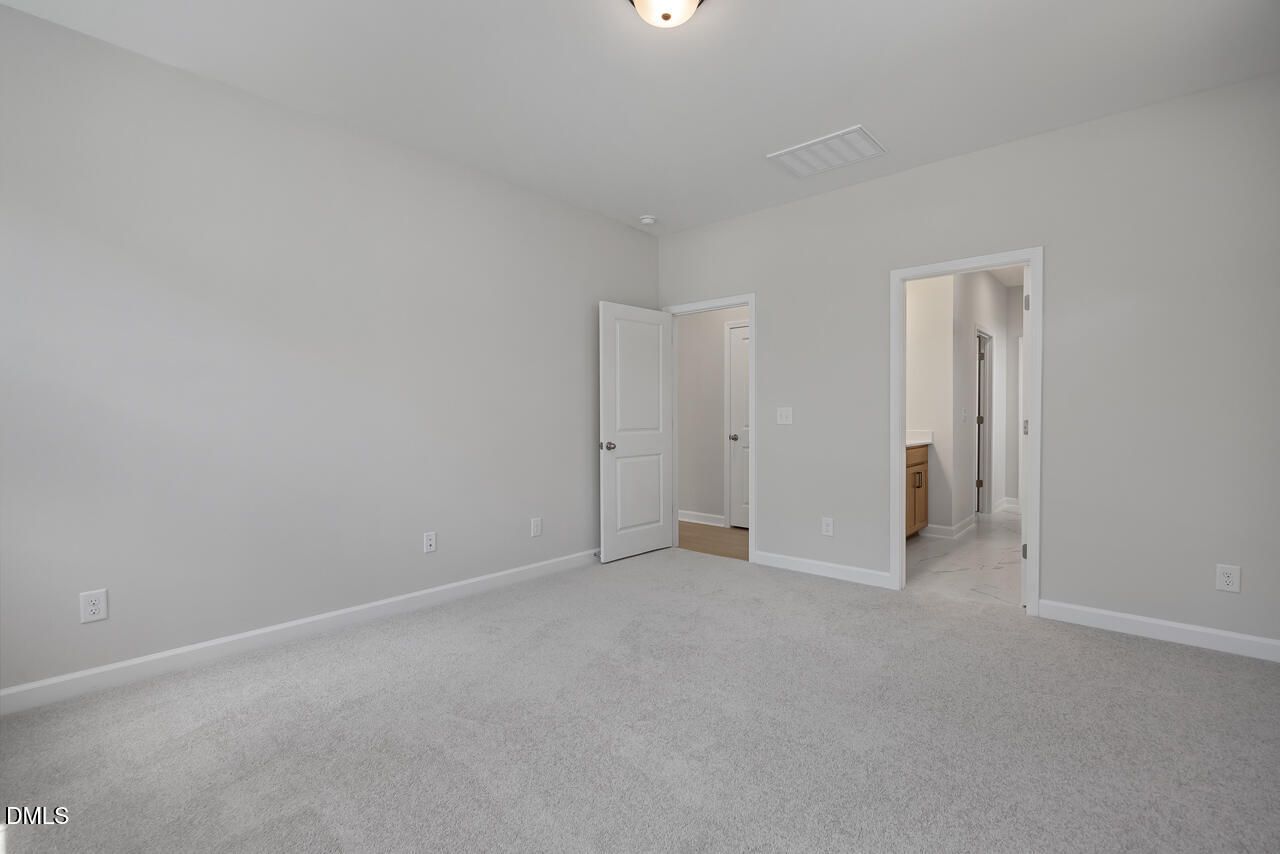 Spacious primary bedroom with neutral carpet and ensuite bathroom in The Ashport L floor plan by Davidson Homes.