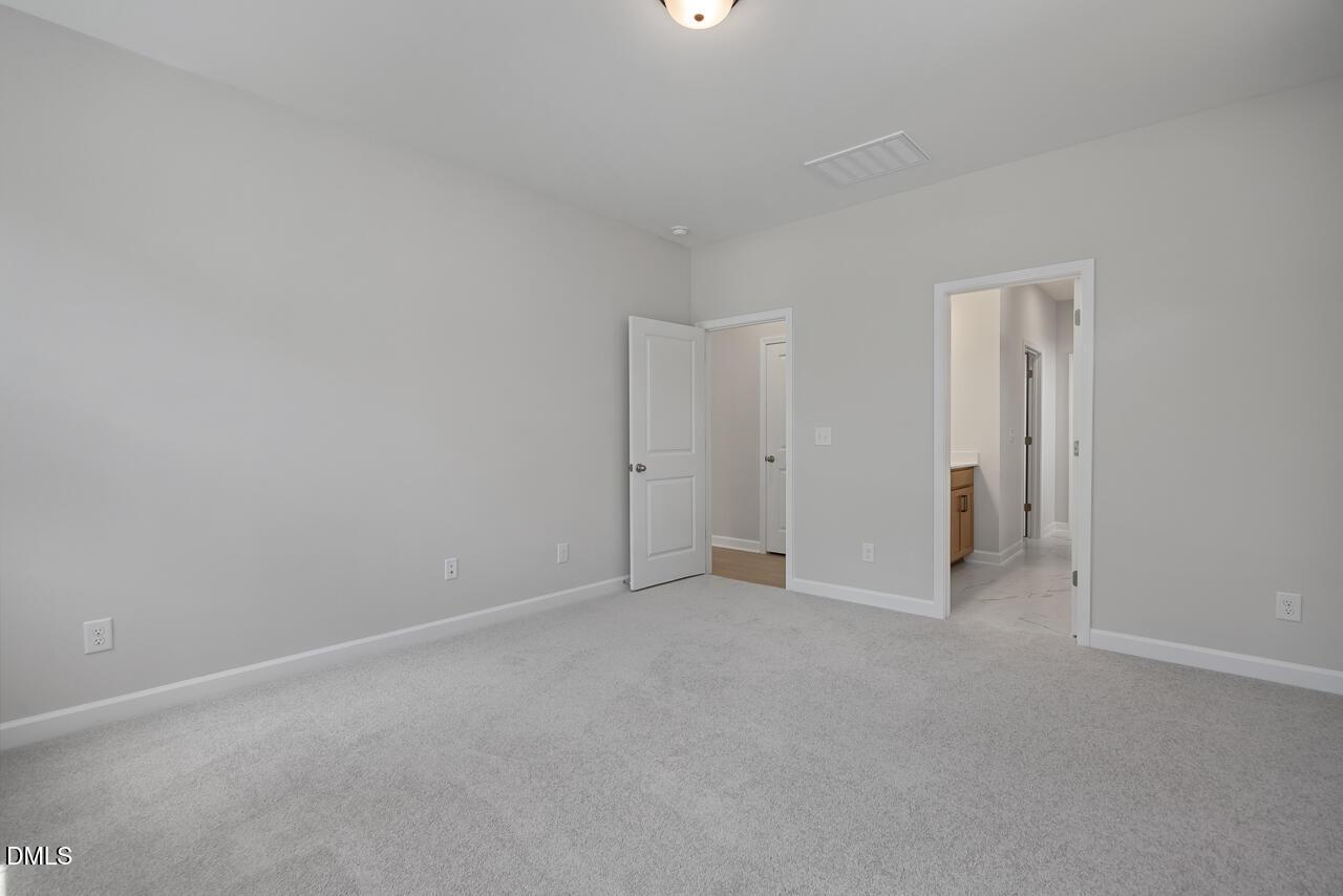 Spacious primary bedroom with neutral carpet and ensuite bathroom in The Ashport L floor plan by Davidson Homes.