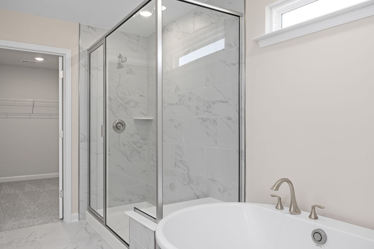 Master suite bathroom in The Chestnut featuring a glass-enclosed shower with marble-look tile and a soaking tub.
