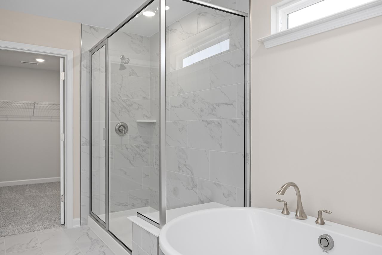 Master suite bathroom in The Chestnut featuring a glass-enclosed shower with marble-look tile and a soaking tub.