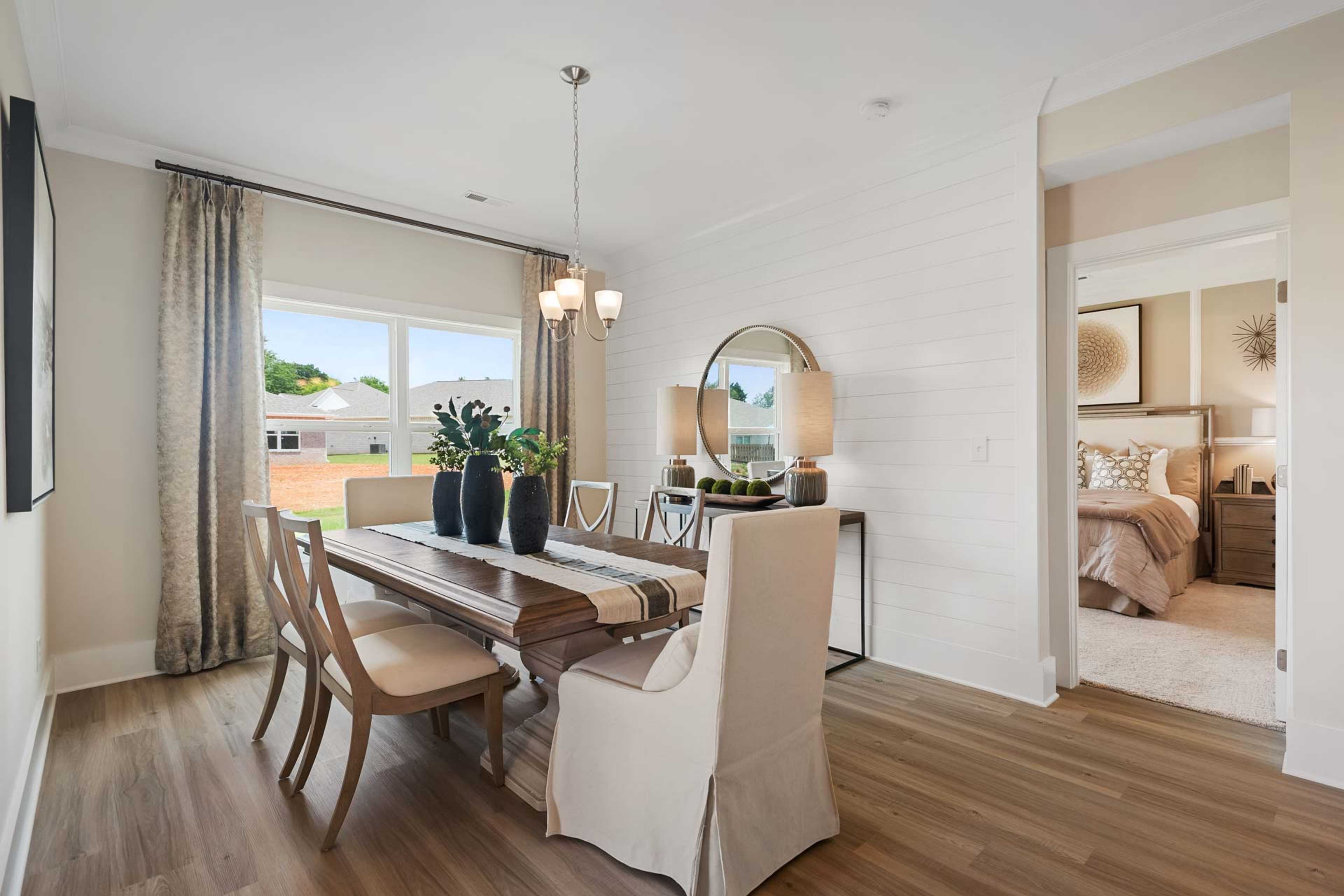 Spacious dining room in Flint Meadows, New Market AL with wooden table, upholstered chairs, chandelier, shiplap walls, and open bedroom view