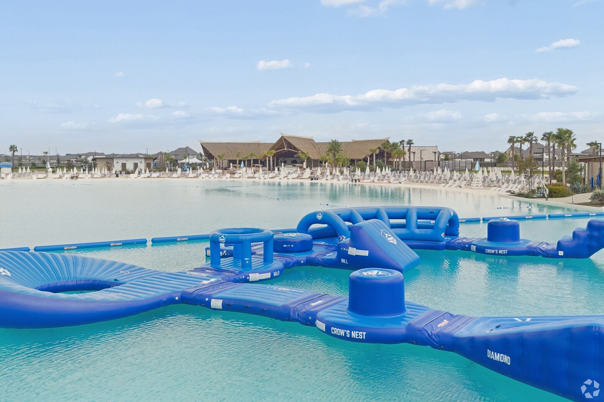 Crystal lagoon with inflatable water obstacle course at River Ranch Meadows in Dayton, Texas with beach loungers and tiki pavilion