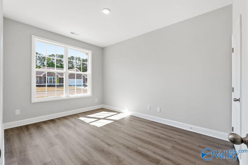 Bright secondary bedroom featuring light gray walls, large sunny window with tree views, gray LVP flooring in Davidson Homes The Harrison, Hartselle AL