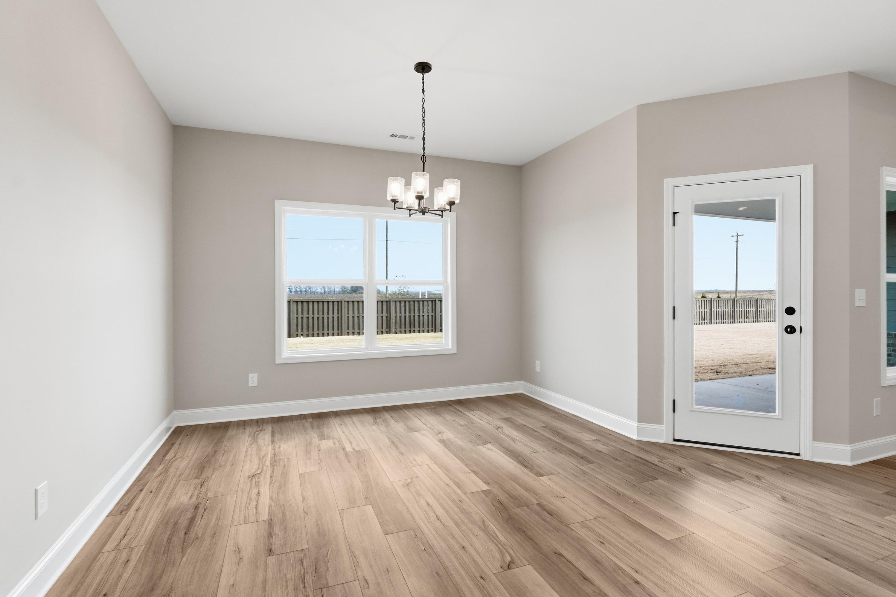 Spacious dining room in The Rockford home by Davidson Homes: light gray walls, oak hardwood floors, modern chandelier, large window, and glass door to patio in Cullman AL