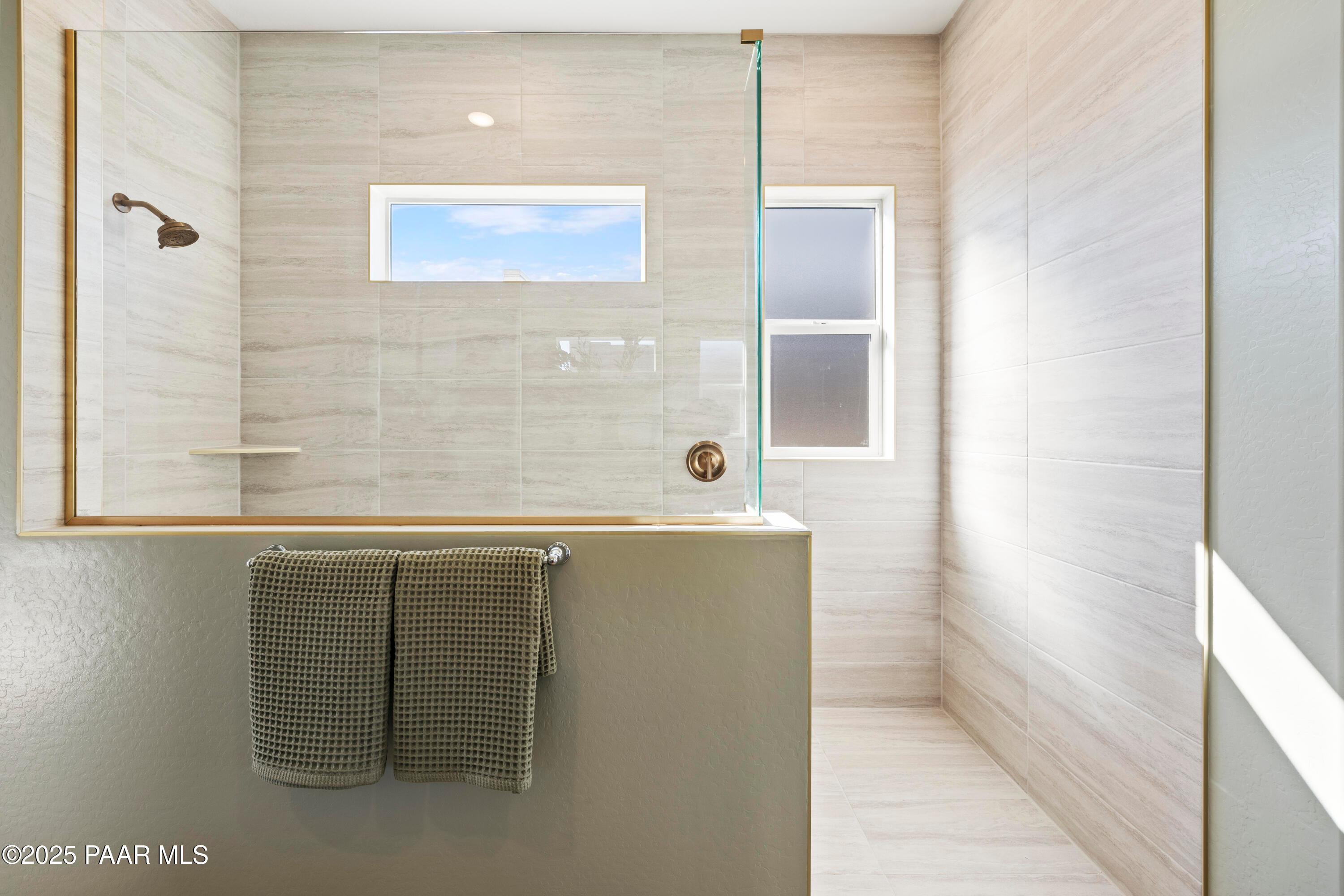 Modern walk-in shower with glass enclosure, beige tiles, and skylight in master bath of The Blaze D home, Hidden Hills, Prescott, Arizona