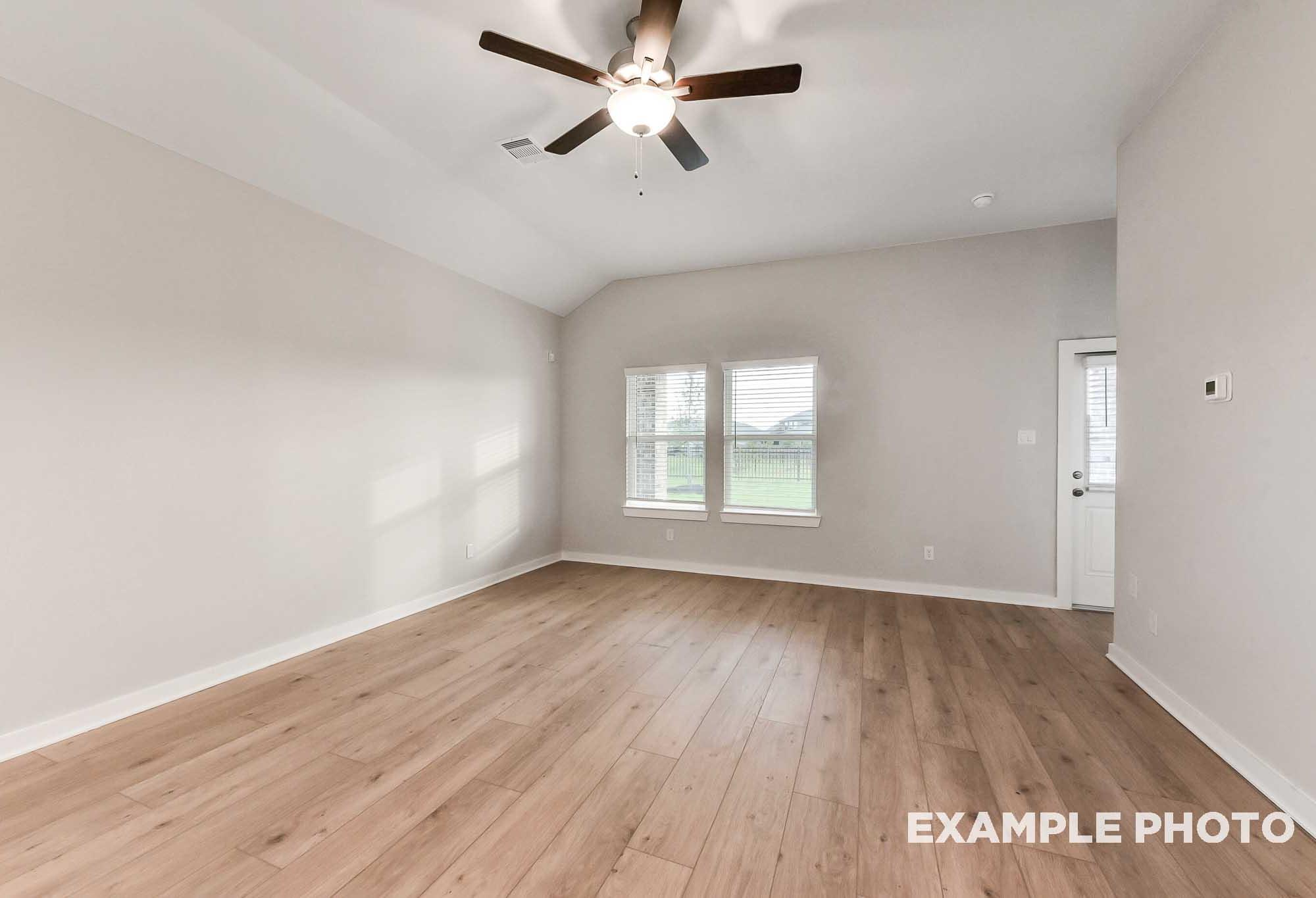 Spacious living room in The Laguna home with light oak laminate floors, ceiling fan, and large windows to green fields