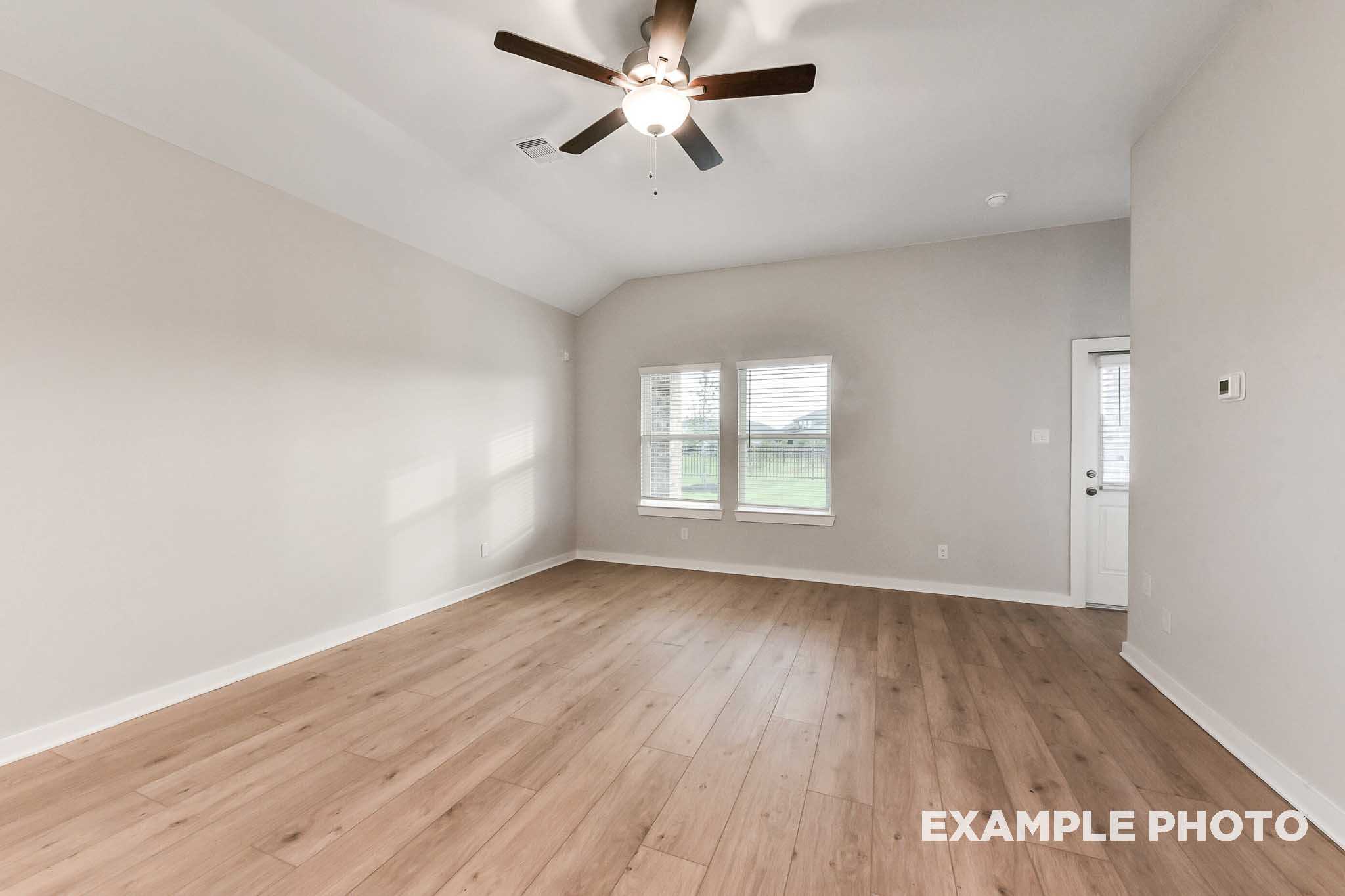 Spacious living room in The Laguna B floor plan featuring light wood floors, neutral walls, ceiling fan, and large windows to green pasture