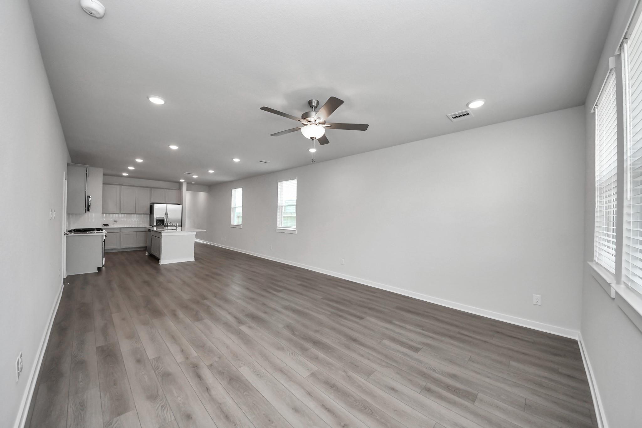 Open-concept living room and kitchen with gray luxury vinyl plank flooring, ceiling fan, and island in Davidson Homes The Frio F, Houston