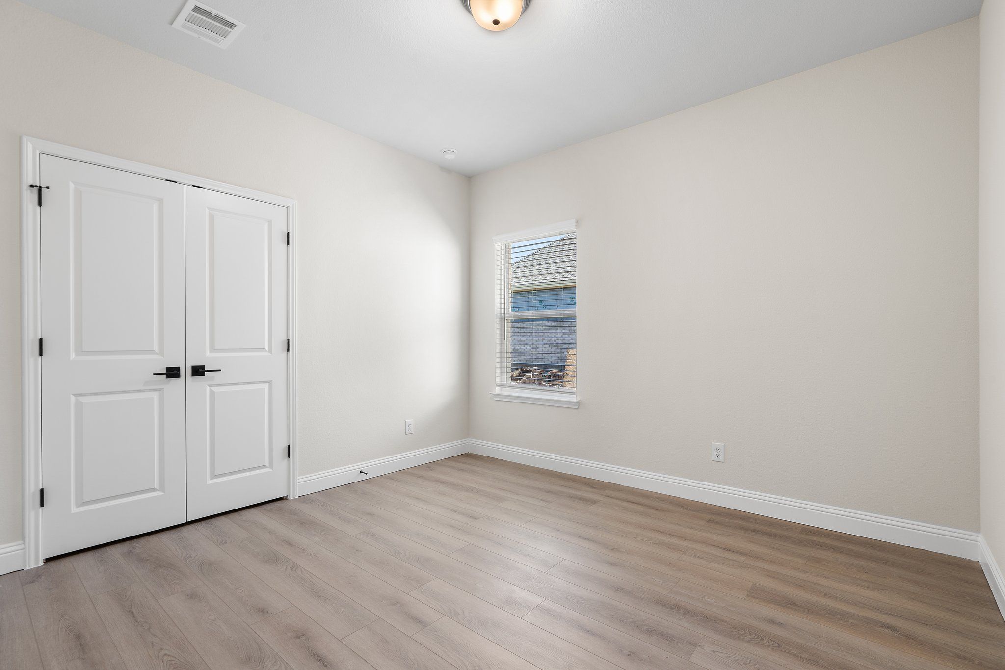 Bright bedroom in The Holly F home design with neutral walls, durable wood-look flooring, and double closet doors.