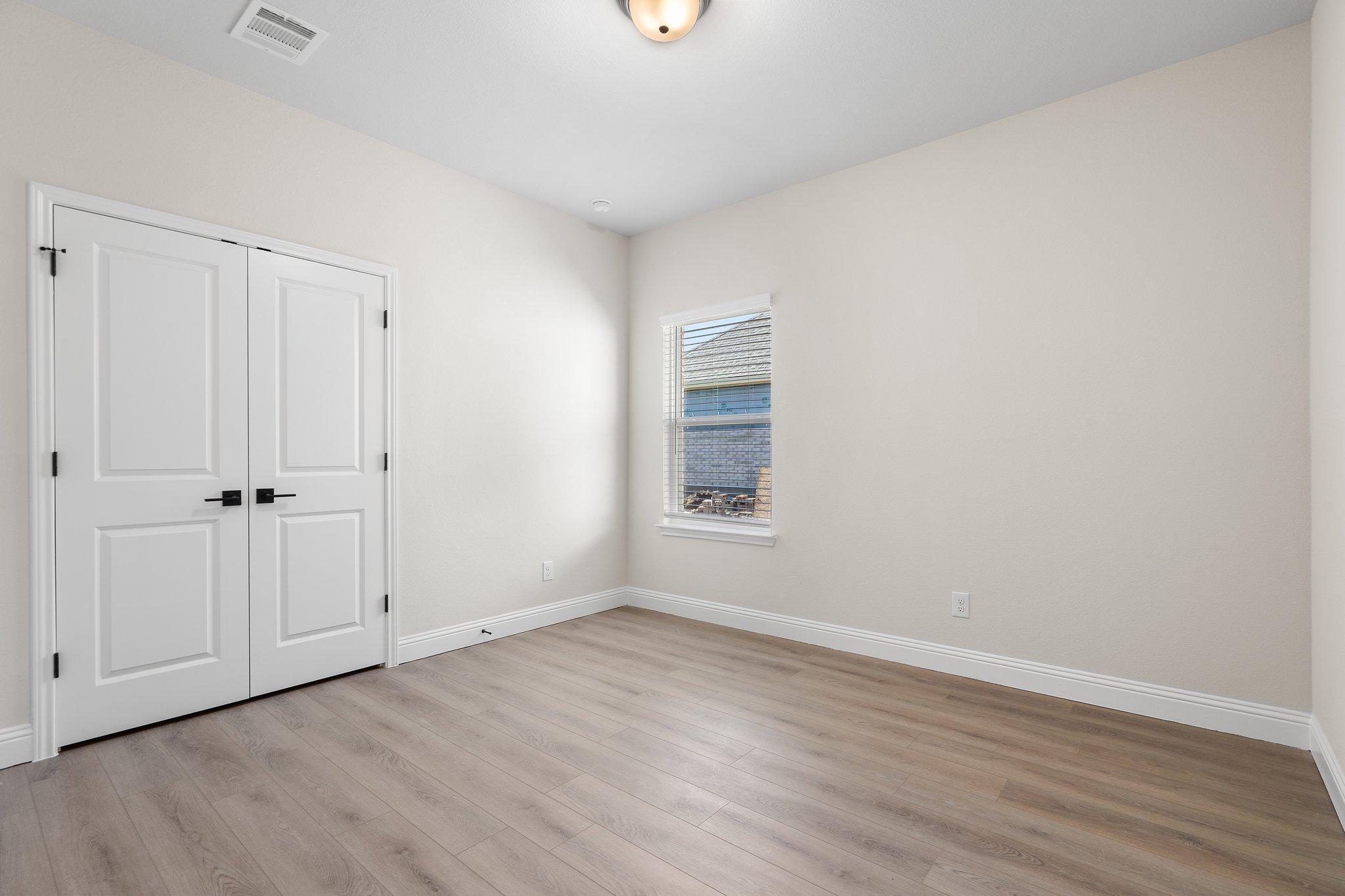 Bright bedroom in The Holly F home design with neutral walls, durable wood-look flooring, and double closet doors.
