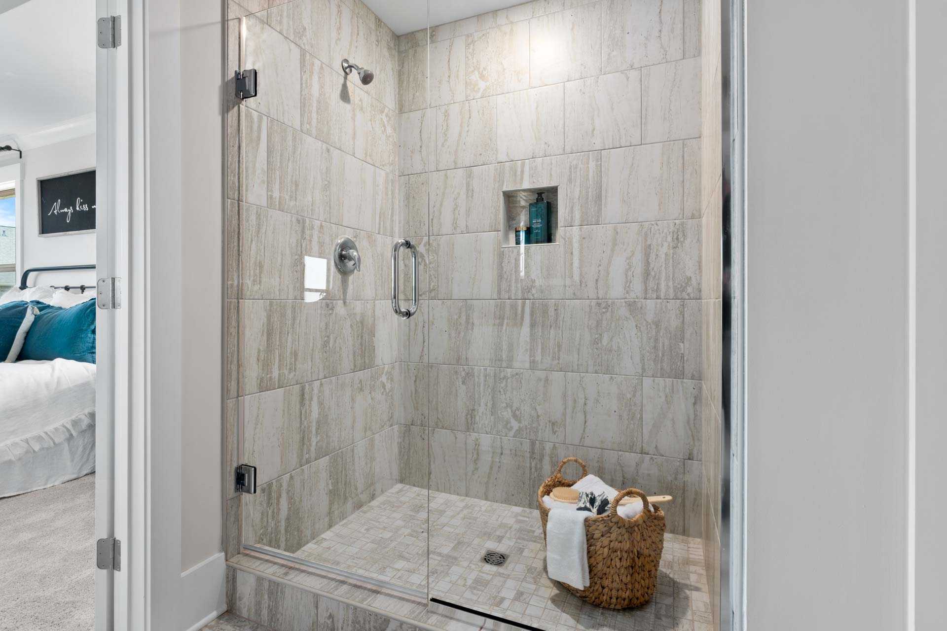 Luxurious walk-in shower at Walker's Hill in Meridianville, Alabama with frameless glass door, stone tile walls, and niche shelf