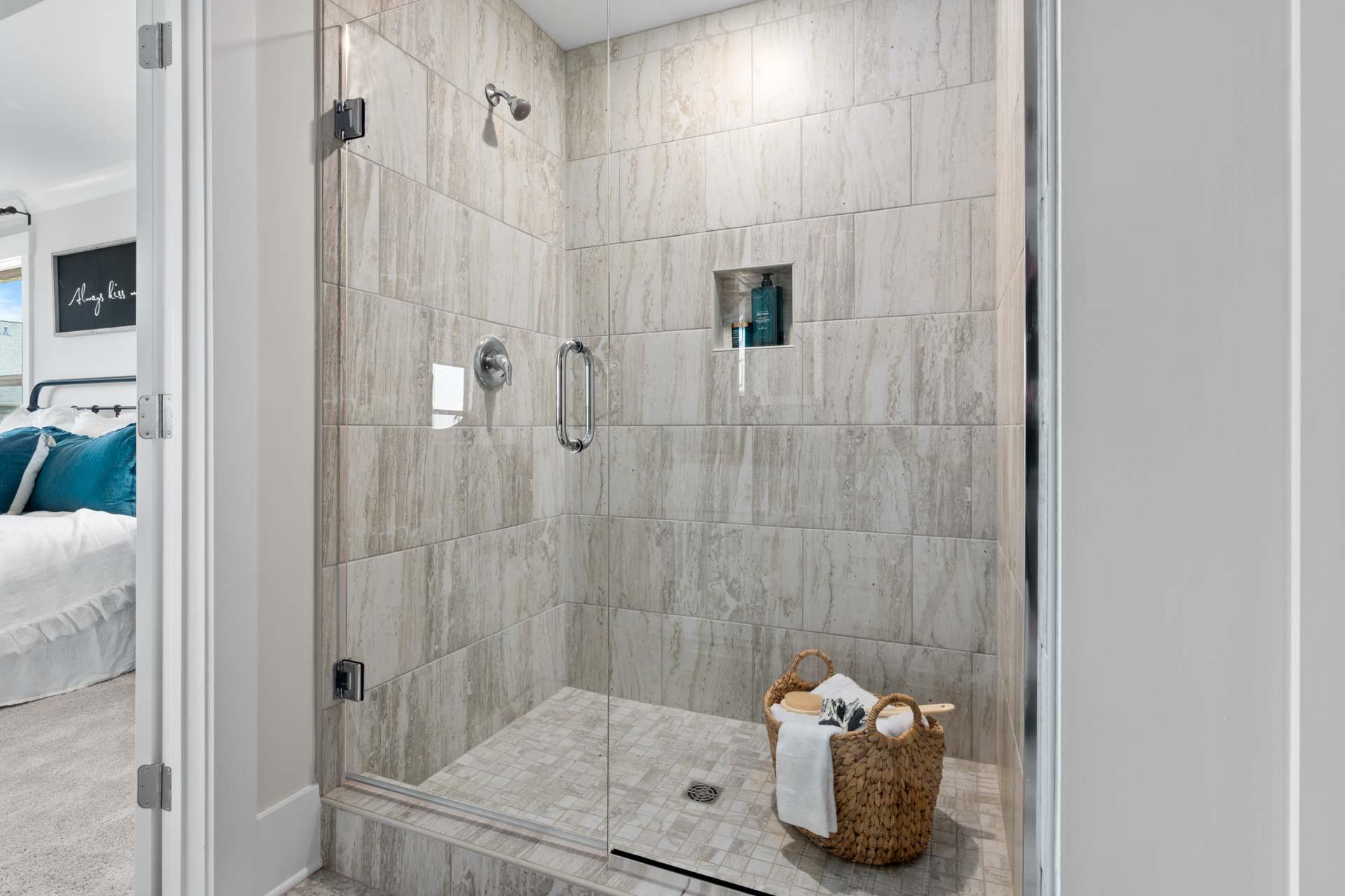 Luxurious walk-in shower at Walker's Hill in Meridianville, Alabama with frameless glass door, stone tile walls, and niche shelf