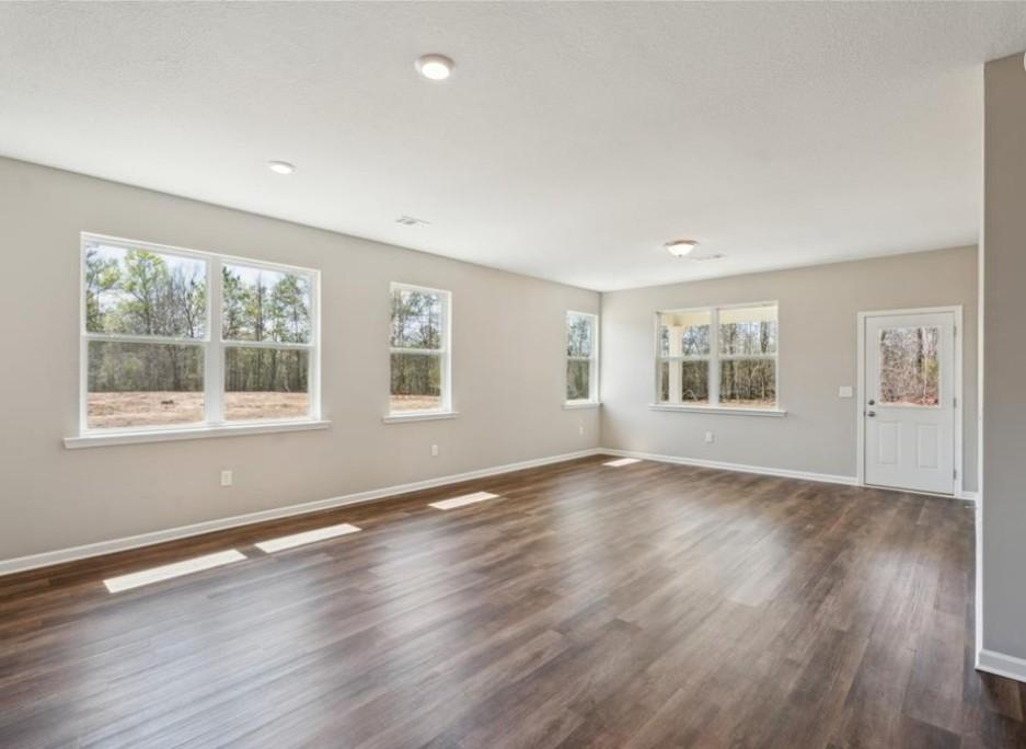 Bright living room with hardwood floors, large windows overlooking trees, and recessed lighting in Evermore Homes The Aurora D, Cusseta, Alabama