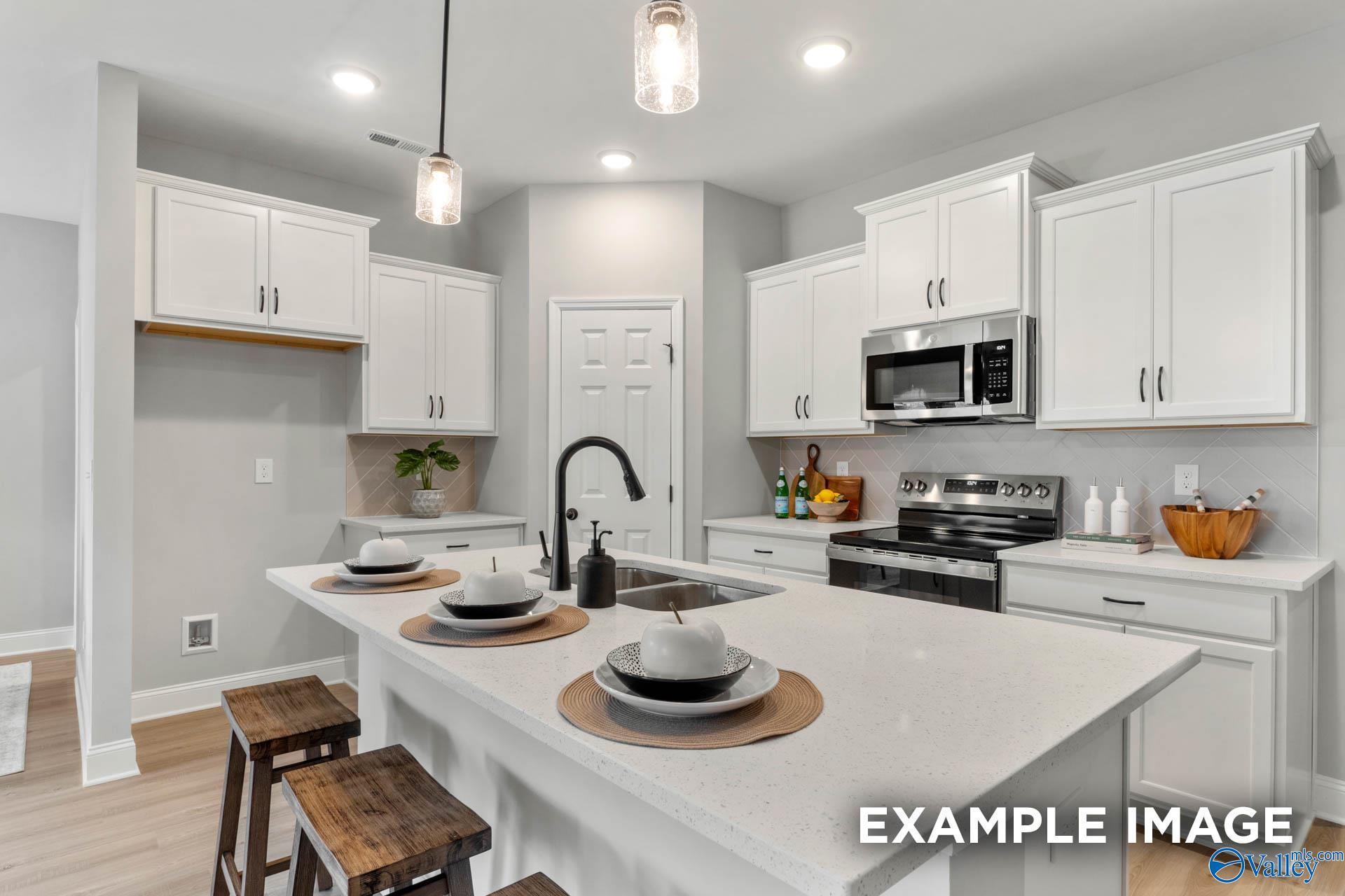 Modern white kitchen with shaker cabinets, quartz island, stainless appliances, black faucet in The Daphne C home, Owens Cross Roads, AL