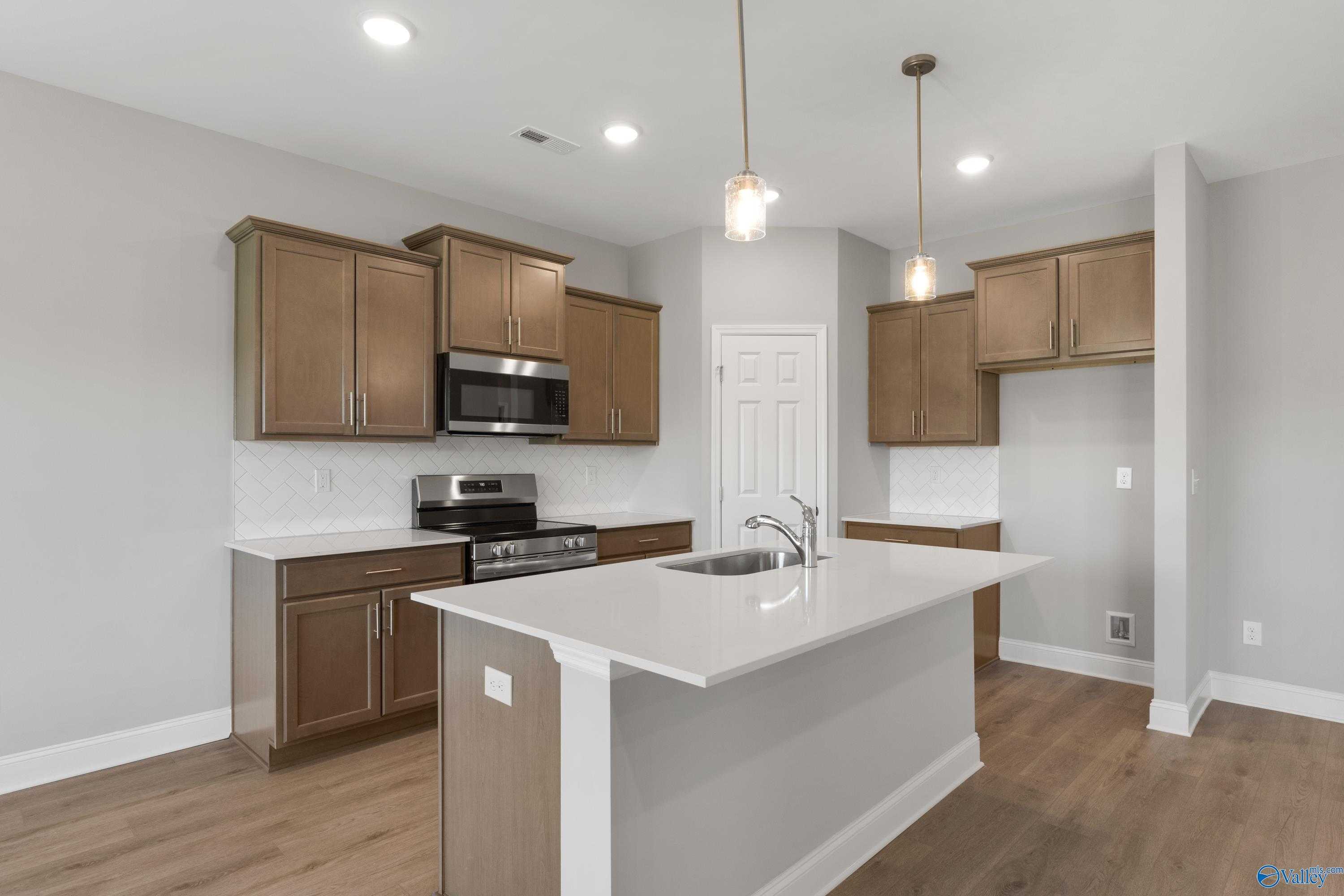 Modern kitchen featuring white quartz island with sink, stainless steel appliances, and warm shaker cabinets in The Asheville C, Athens, AL