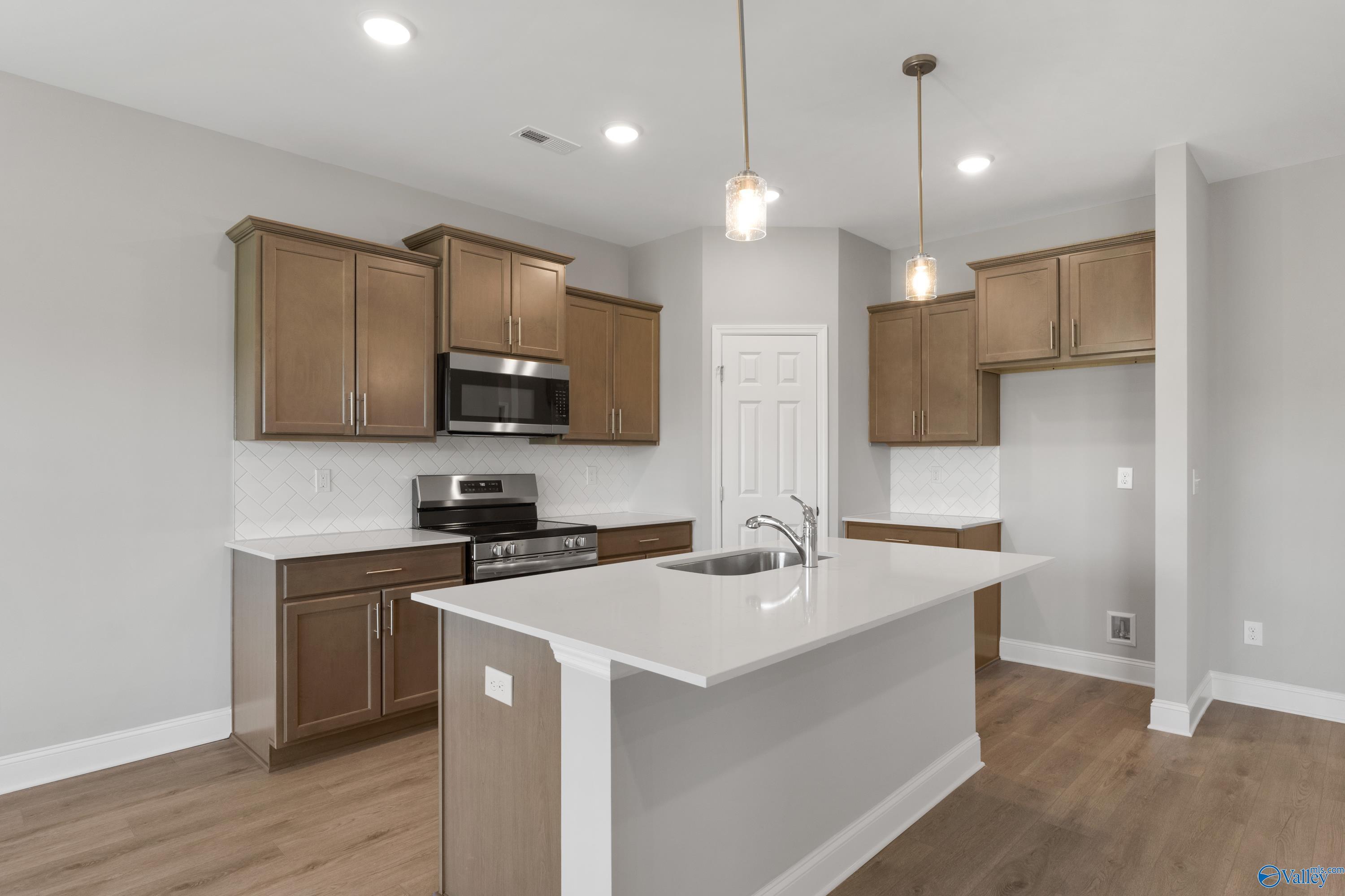 Modern kitchen featuring white quartz island with sink, stainless steel appliances, and warm shaker cabinets in The Asheville C, Athens, AL