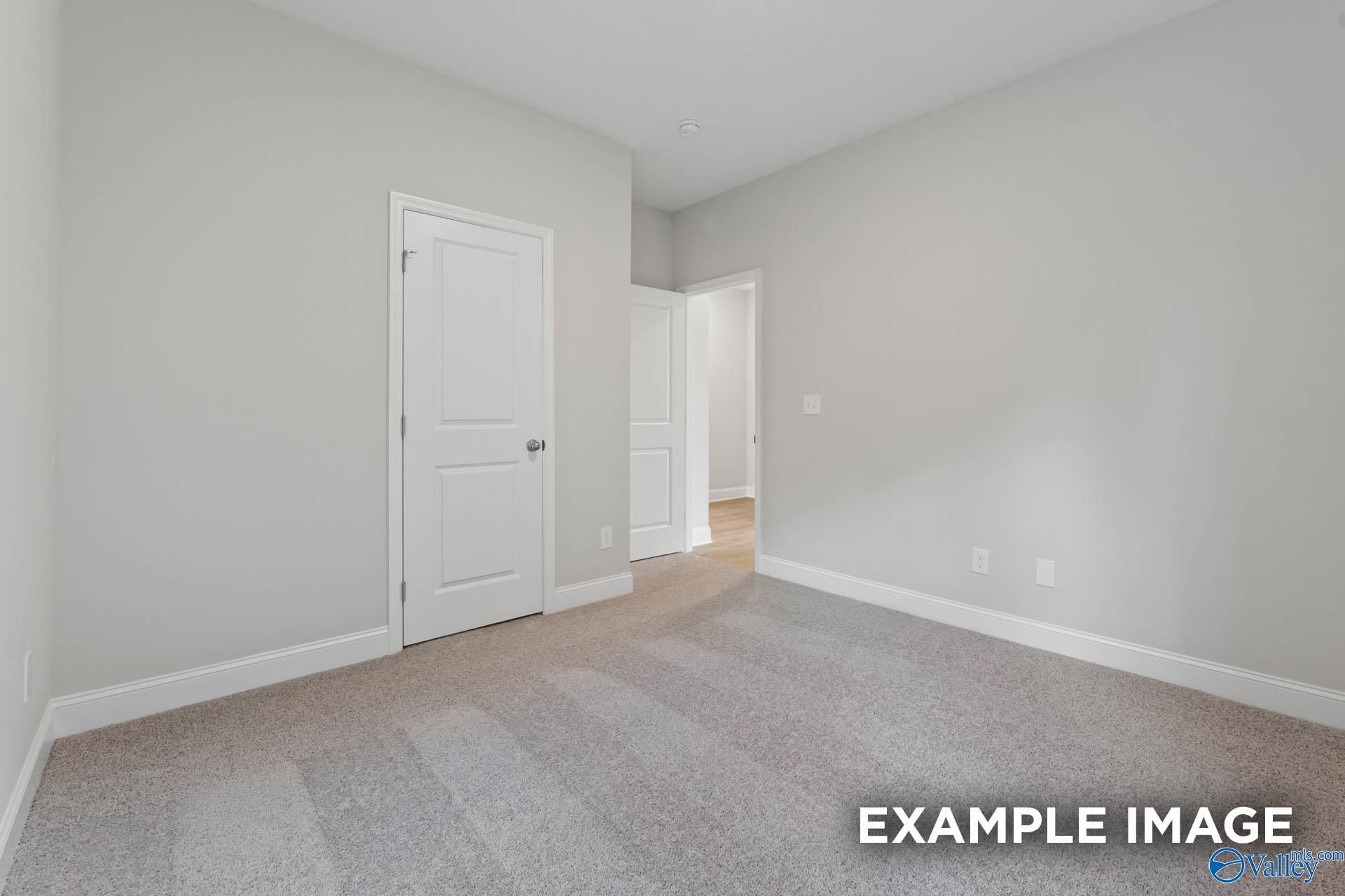 Spacious empty bedroom with light gray walls, neutral carpet, white doors in Davidson Homes The Franklin V, Athens, Alabama