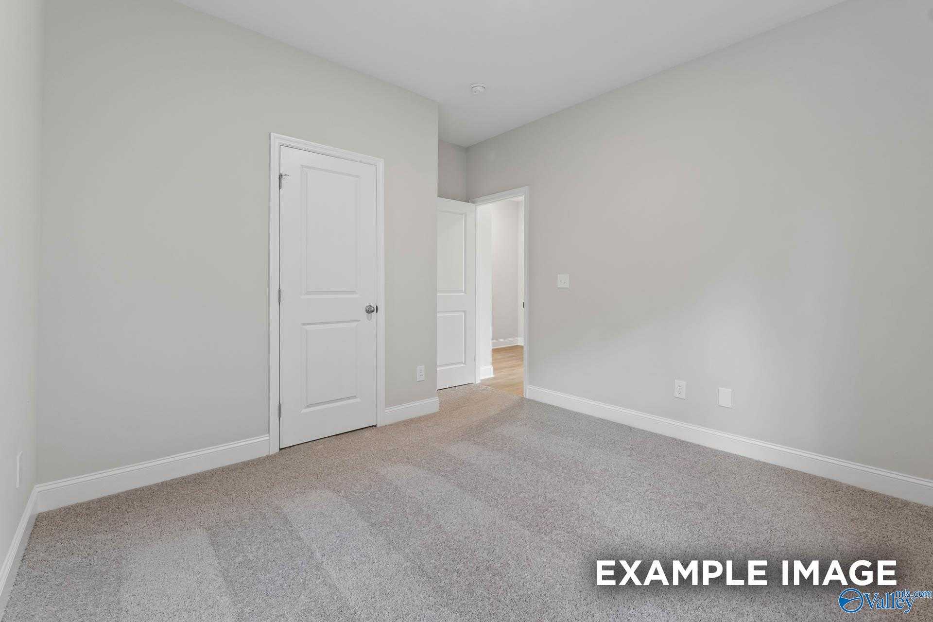 Spacious empty bedroom with light gray walls, neutral carpet, white doors in Davidson Homes The Franklin V, Athens, Alabama
