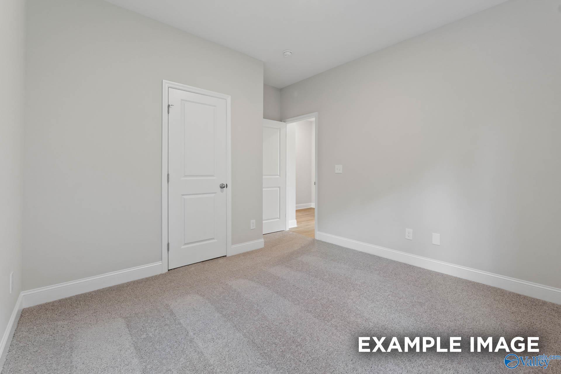 Spacious empty bedroom with light gray walls, neutral carpet, white doors in Davidson Homes The Franklin V, Athens, Alabama