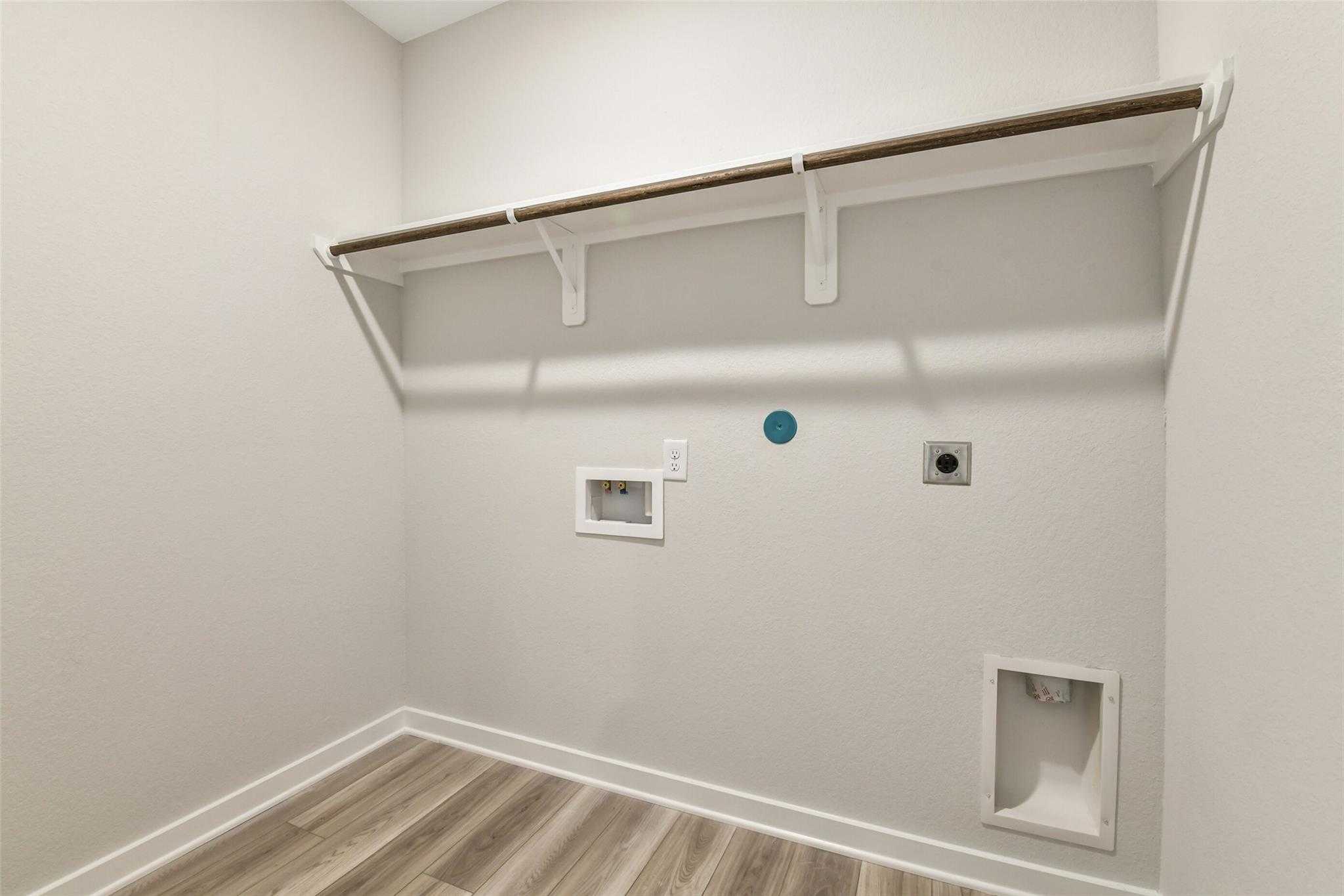 Functional laundry room with floating wood shelves, washer-dryer hookups on light gray walls in Davidson Homes The Daphne H, Crosby Texas