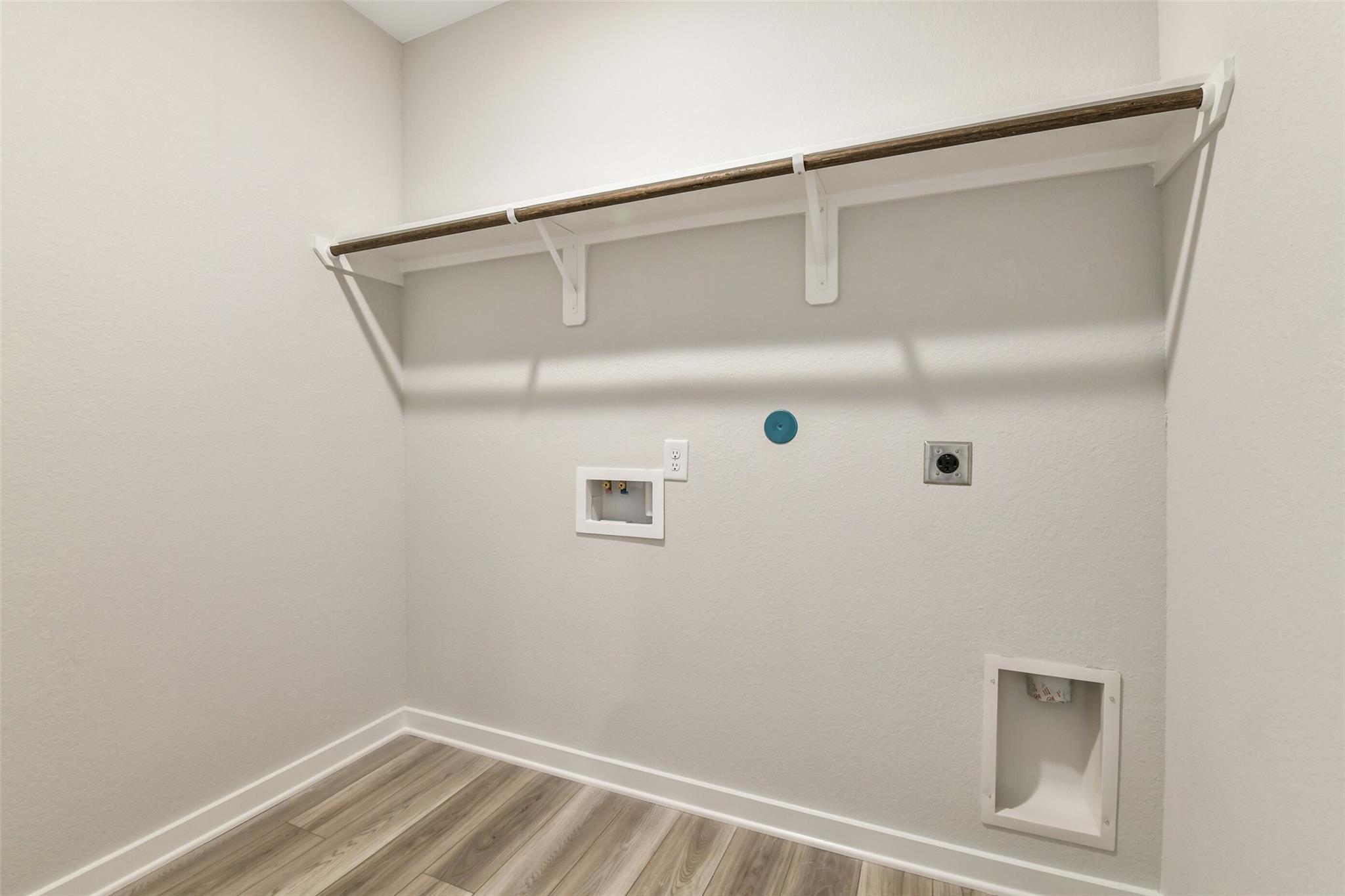 Functional laundry room with floating wood shelves, washer-dryer hookups on light gray walls in Davidson Homes The Daphne H, Crosby Texas