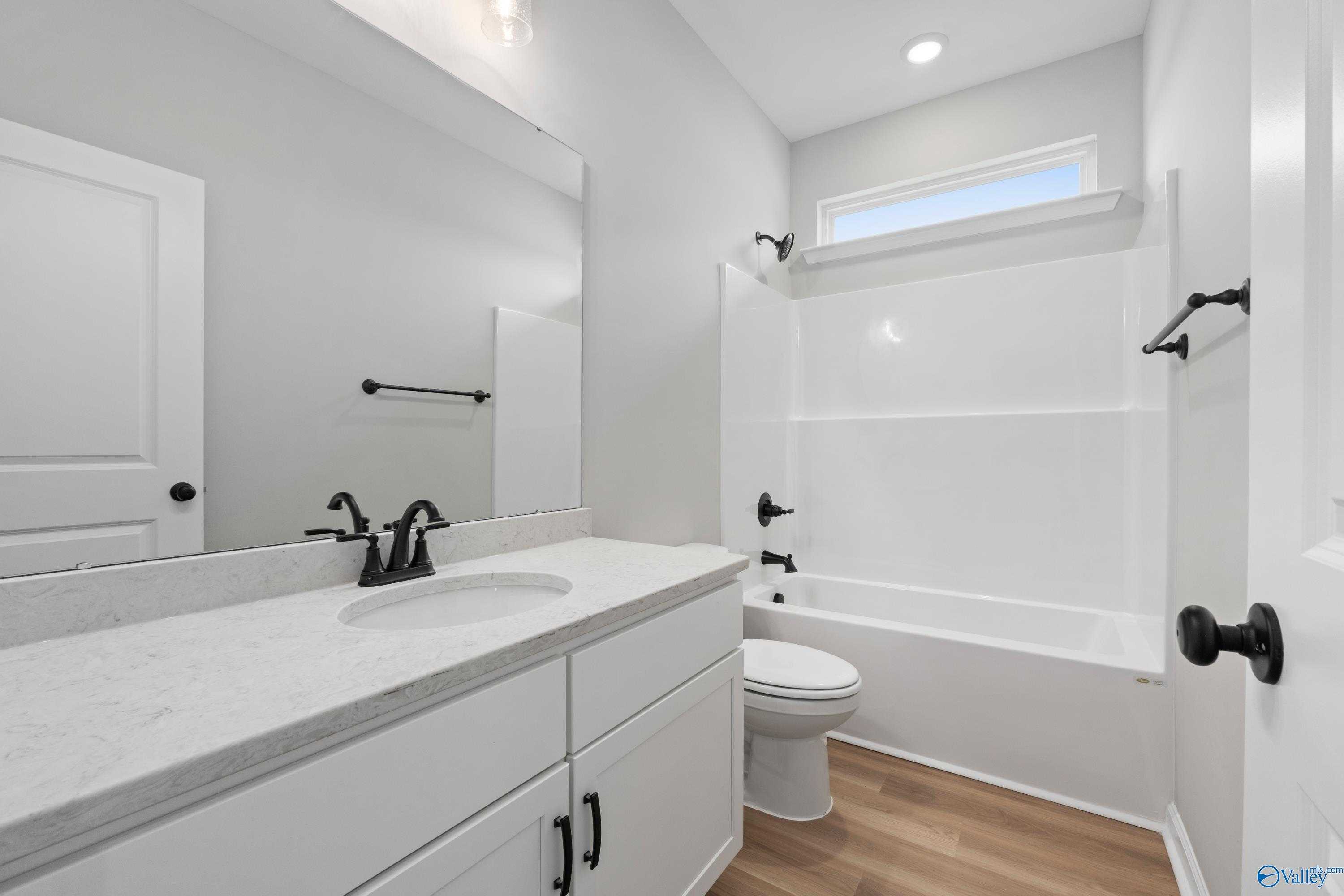 Modern guest bathroom featuring white subway tile shower, quartz vanity, black fixtures, and tub in Evermore Homes The Nantucket, Madison, Alabama