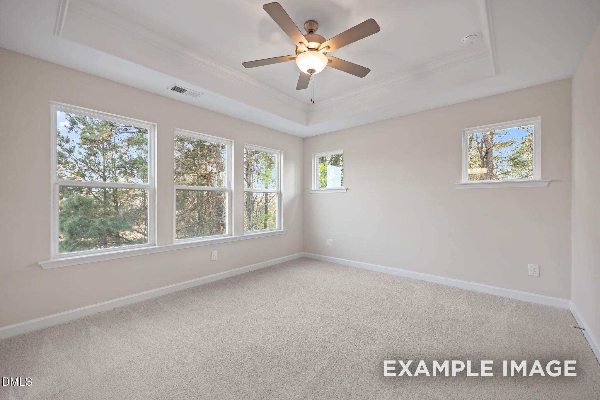 Bright empty bedroom with tray ceiling, ceiling fan, and large windows overlooking pines in Davidson Homes The Avery, Knightdale NC