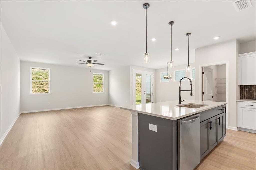 Open-concept kitchen with white cabinets, gray island sink, stainless dishwasher, and pendant lights in The Daphne C, Loganville, GA