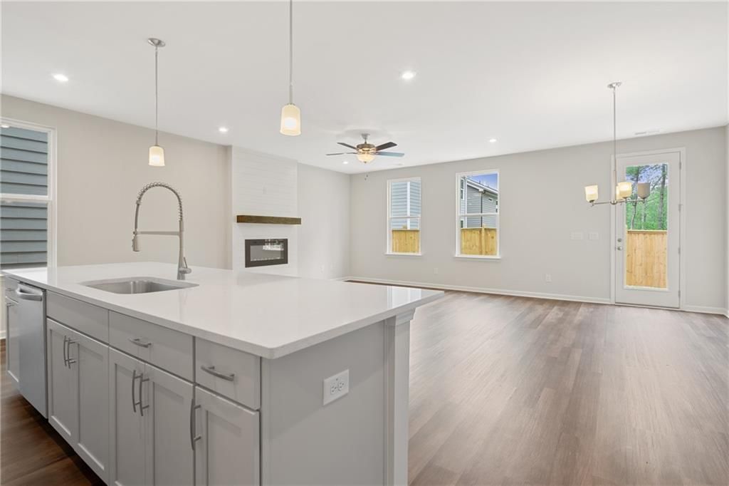 Modern open kitchen with white quartz island, farmhouse sink, and adjacent living room featuring gas fireplace in The Cary B, Kennesaw, GA