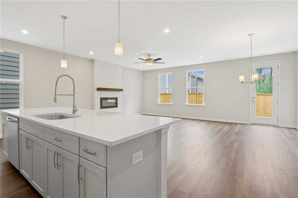 Modern open kitchen with white quartz island, farmhouse sink, and adjacent living room featuring gas fireplace in The Cary B, Kennesaw, GA