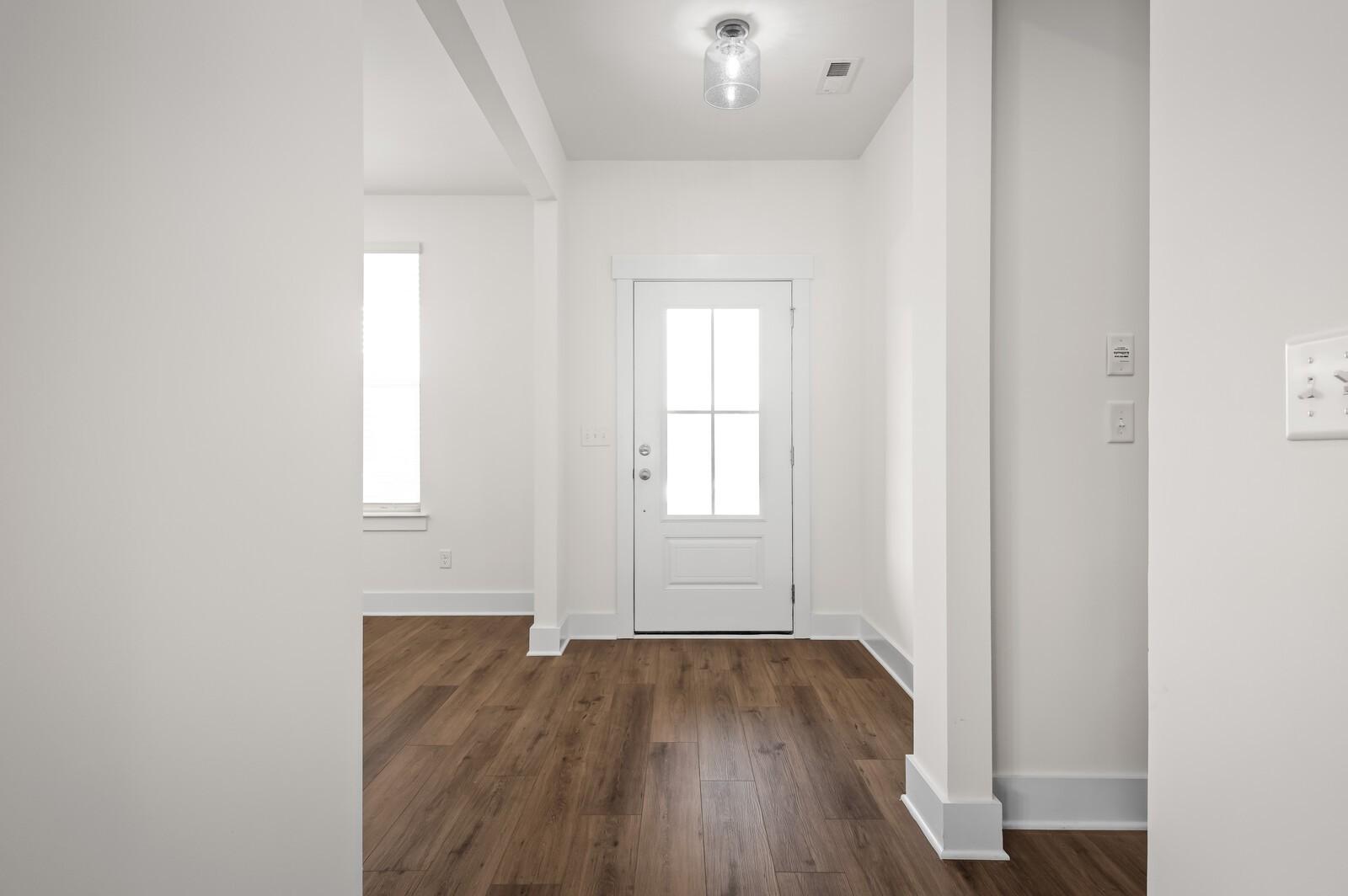 Bright entryway with wood-style flooring and glass-paneled front door in The Ash A home at Woods Crossing, Gallatin, TN.