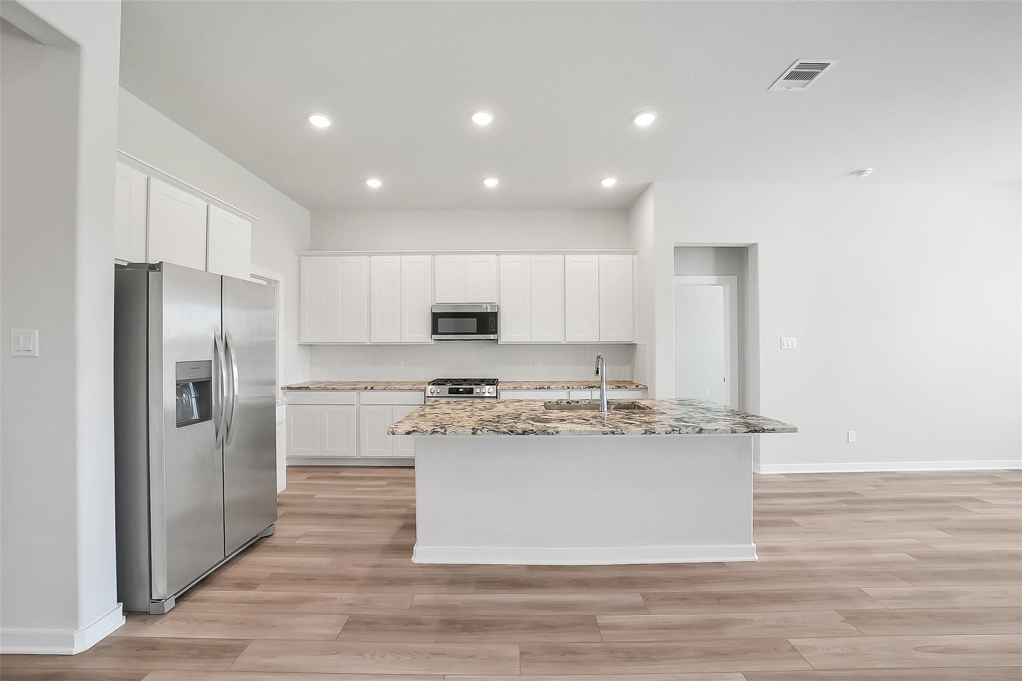 Modern kitchen with white cabinets, stainless steel fridge, granite island, and open layout in Davidson Homes The Acadia A, Katy, Texas