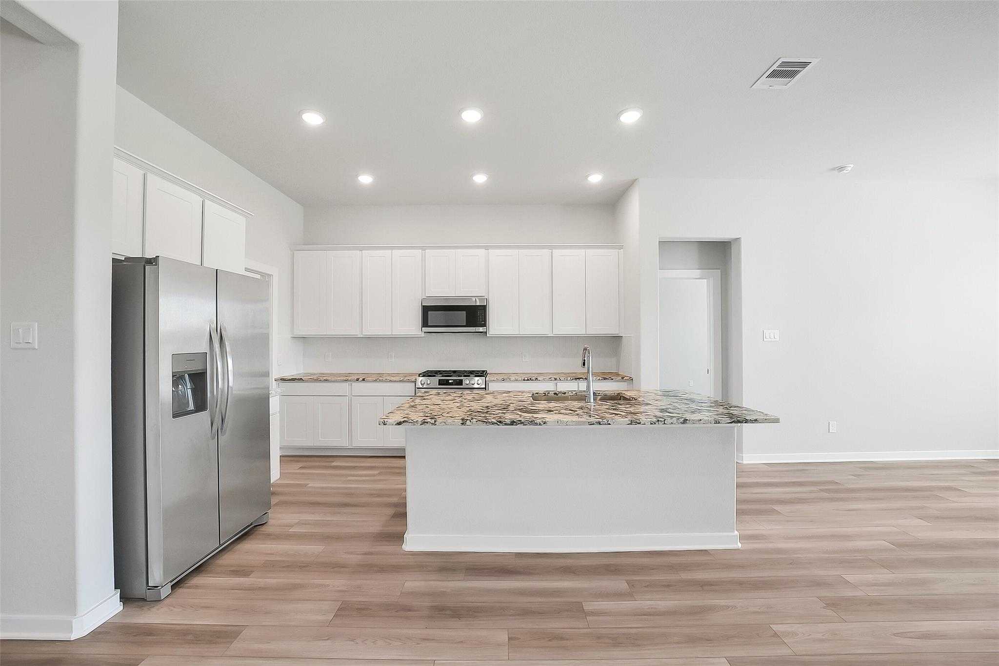 Modern kitchen with white cabinets, stainless steel fridge, granite island, and open layout in Davidson Homes The Acadia A, Katy, Texas