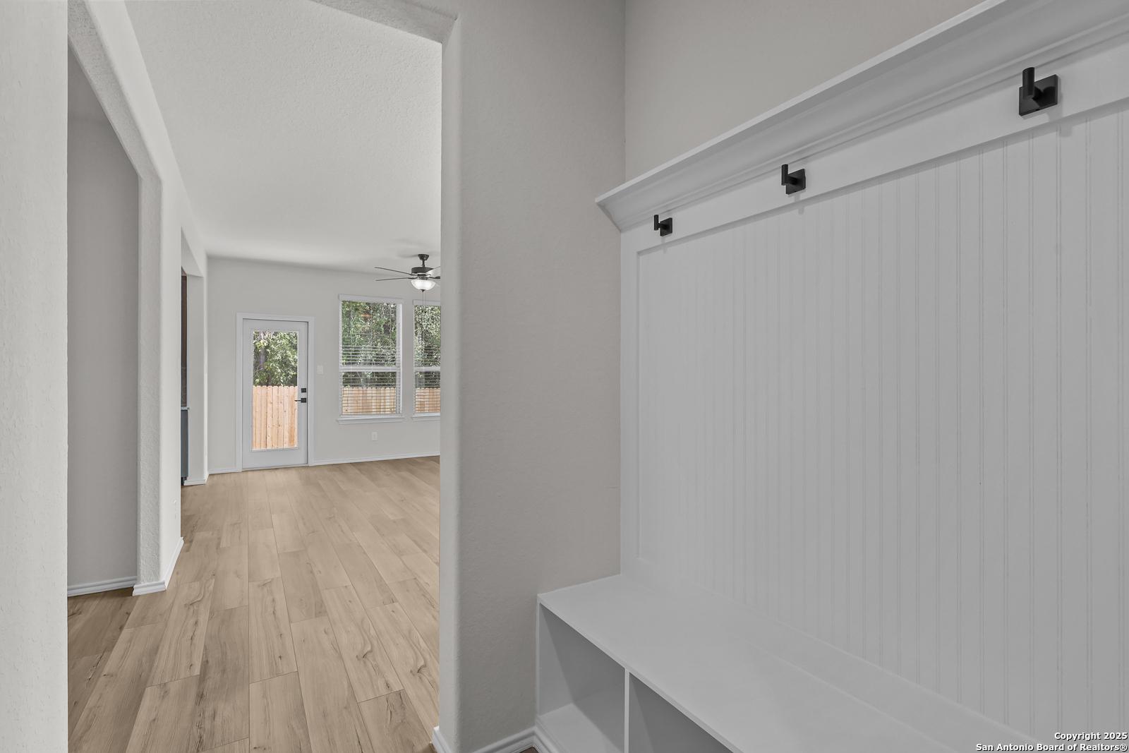 Welcoming entryway with white shiplap bench, coat hooks, and open hallway featuring hardwood floors in Davidson Homes The Florence C, San Antonio
