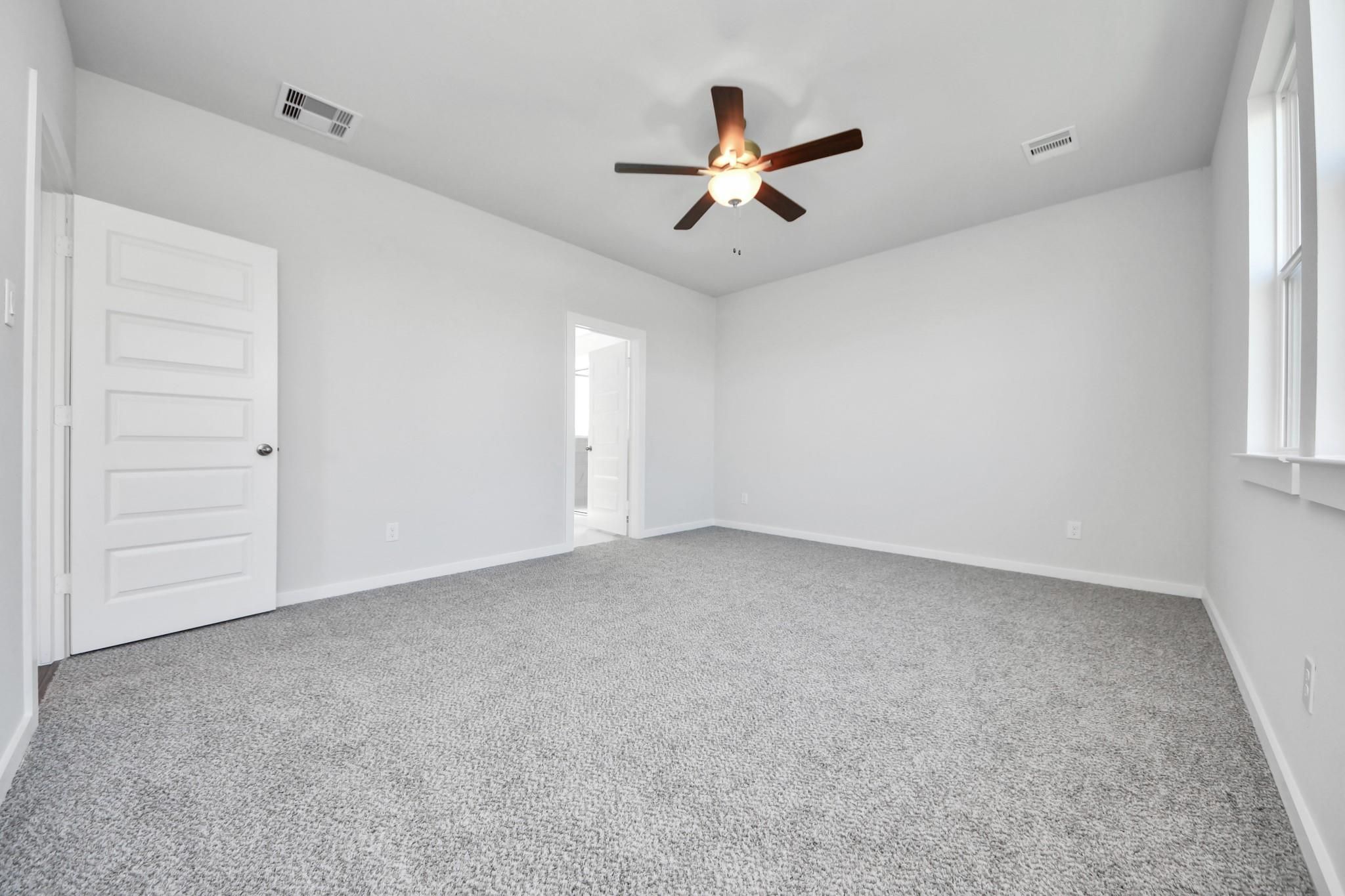 Bright, carpeted bedroom with ceiling fan in The Riviera A floor plan at Emberly, Beasley, Texas.