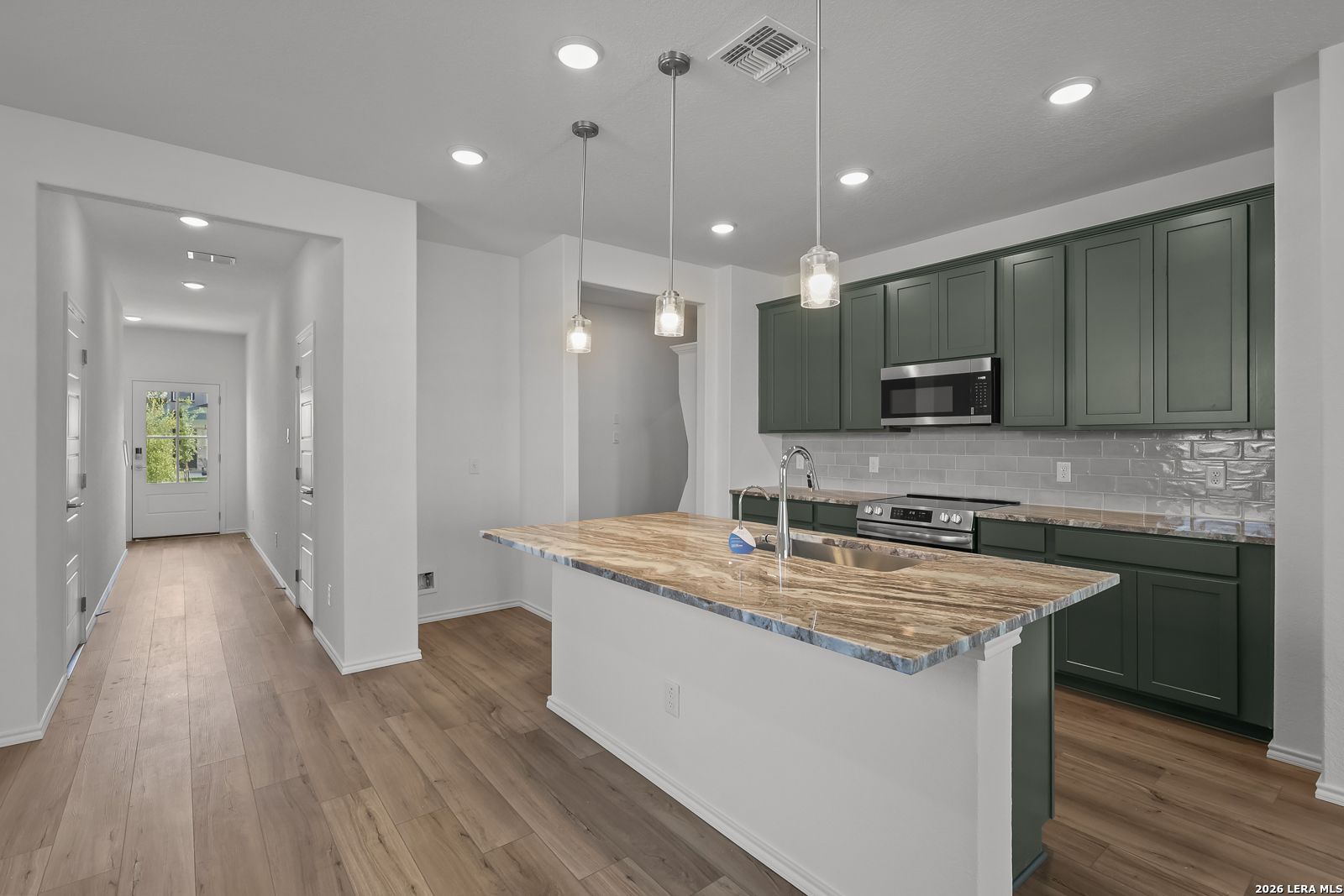 Modern kitchen with dark green cabinets and stone island in The Brazos B home at Agave, San Antonio, Texas.