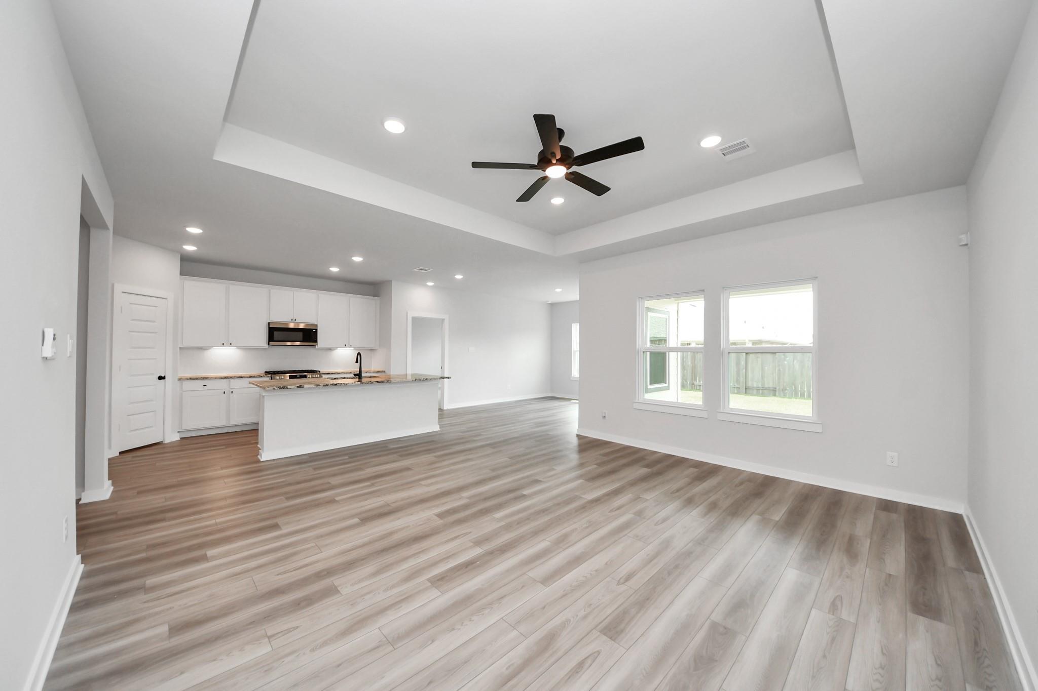 Open-concept living room and kitchen with tray ceiling in The Everett C floor plan at River Ranch Meadows, Dayton, Texas.