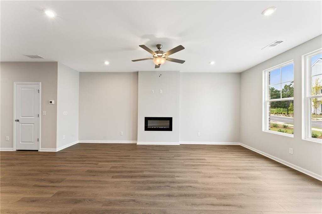 Bright living room with modern gas fireplace, ceiling fan, hardwood floors, and large windows in Davidson Homes The Monroe A, Emerson, GA