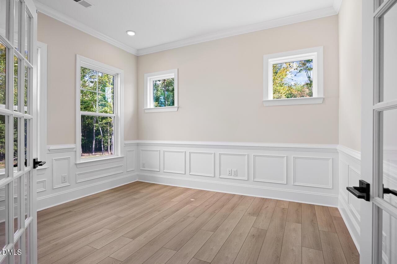 Bright empty room with wainscoting, wood-look flooring, and garden views in Davidson Homes Crawford D plan, Wake Forest, NC