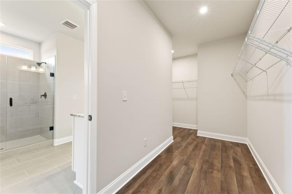 Spacious master walk-in closet with wire shelving and hardwood floors adjacent to frameless glass shower bathroom in Davidson Homes The Harrison G, Hoschton GA