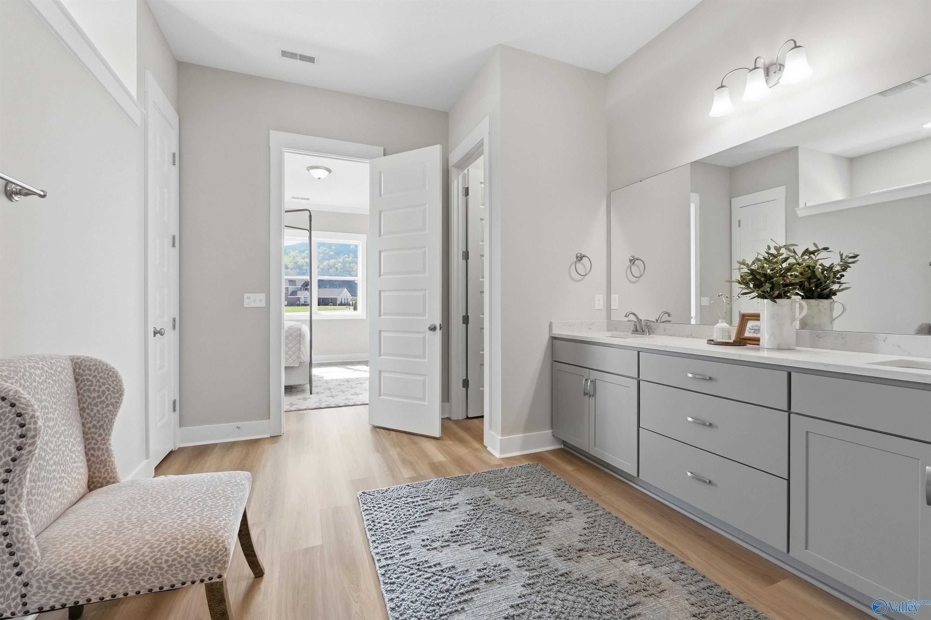 Elegant master bathroom double vanity with gray cabinets, quartz counters, and open bedroom view in Evermore Homes The Oxford B, Owens Cross Roads, Alabama