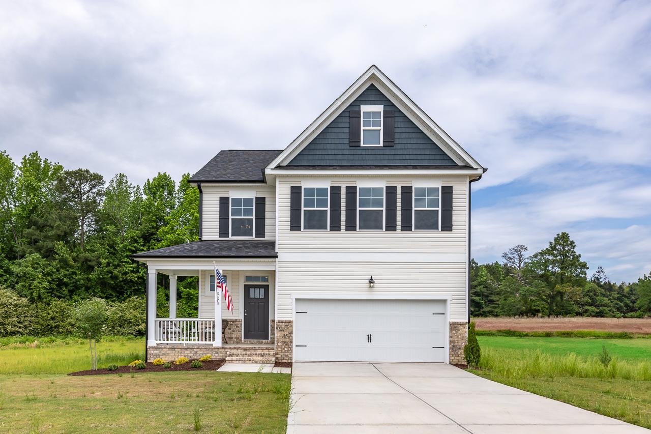 Charming two-story home exterior at Wellers Knoll in Lillington NC with covered front porch, attached garage, and lush green yard