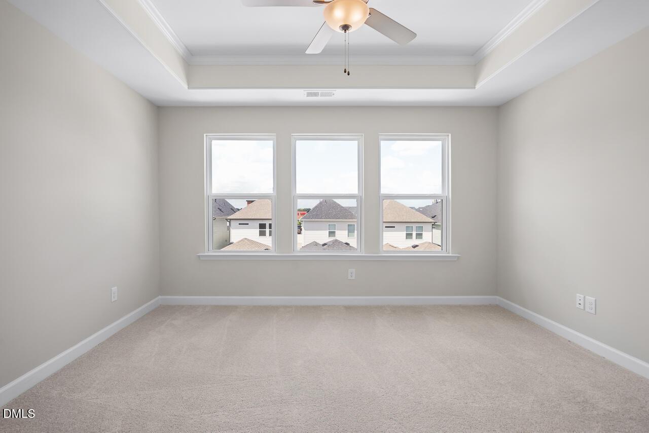 Bright bedroom with tray ceiling, ceiling fan, and triple windows overlooking Forestville Yard Townhomes in Knightdale, North Carolina