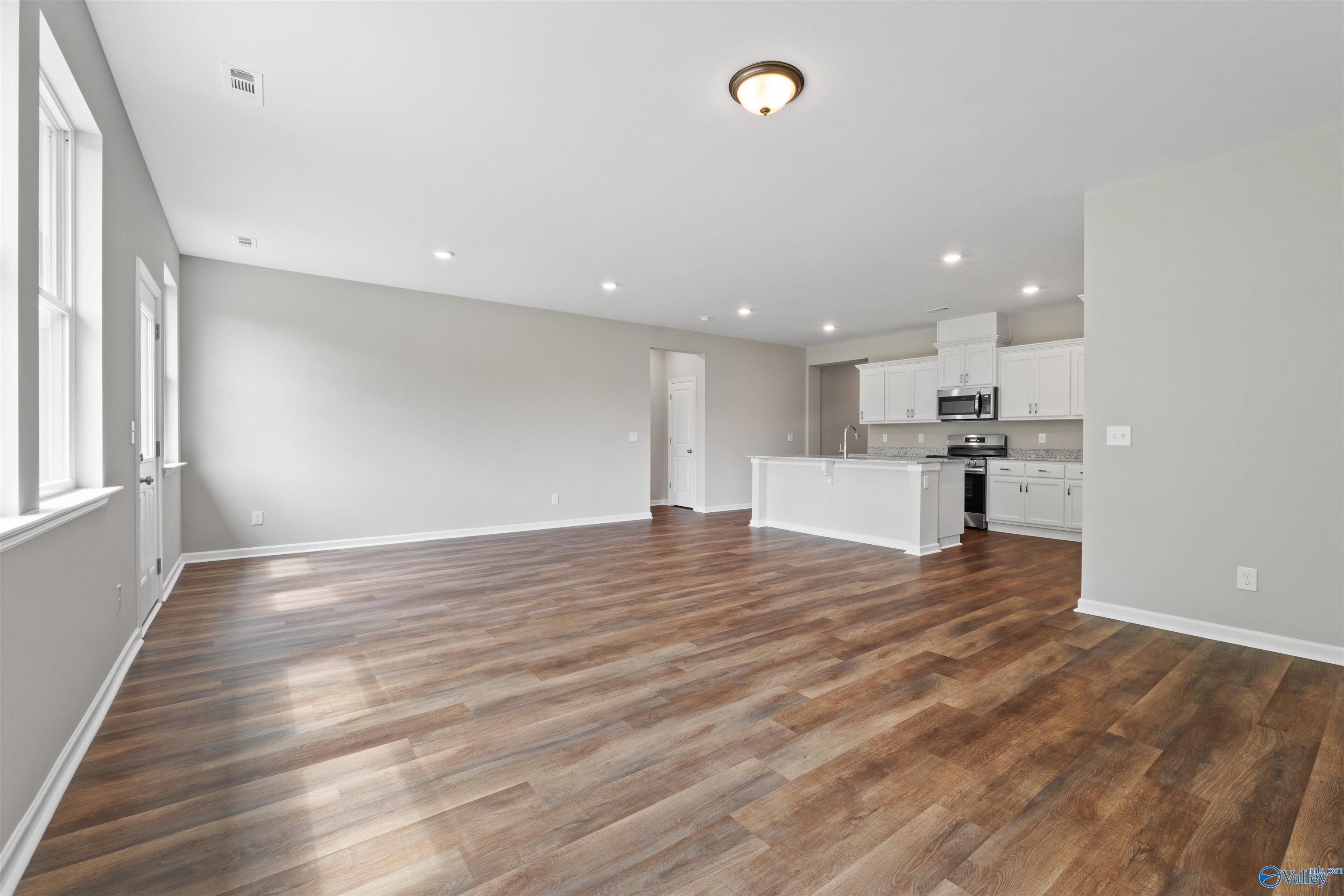 Open-concept kitchen and living area with hardwood floors, white cabinets, and stainless appliances in Davidson Homes The Luna, Hazel Green, AL
